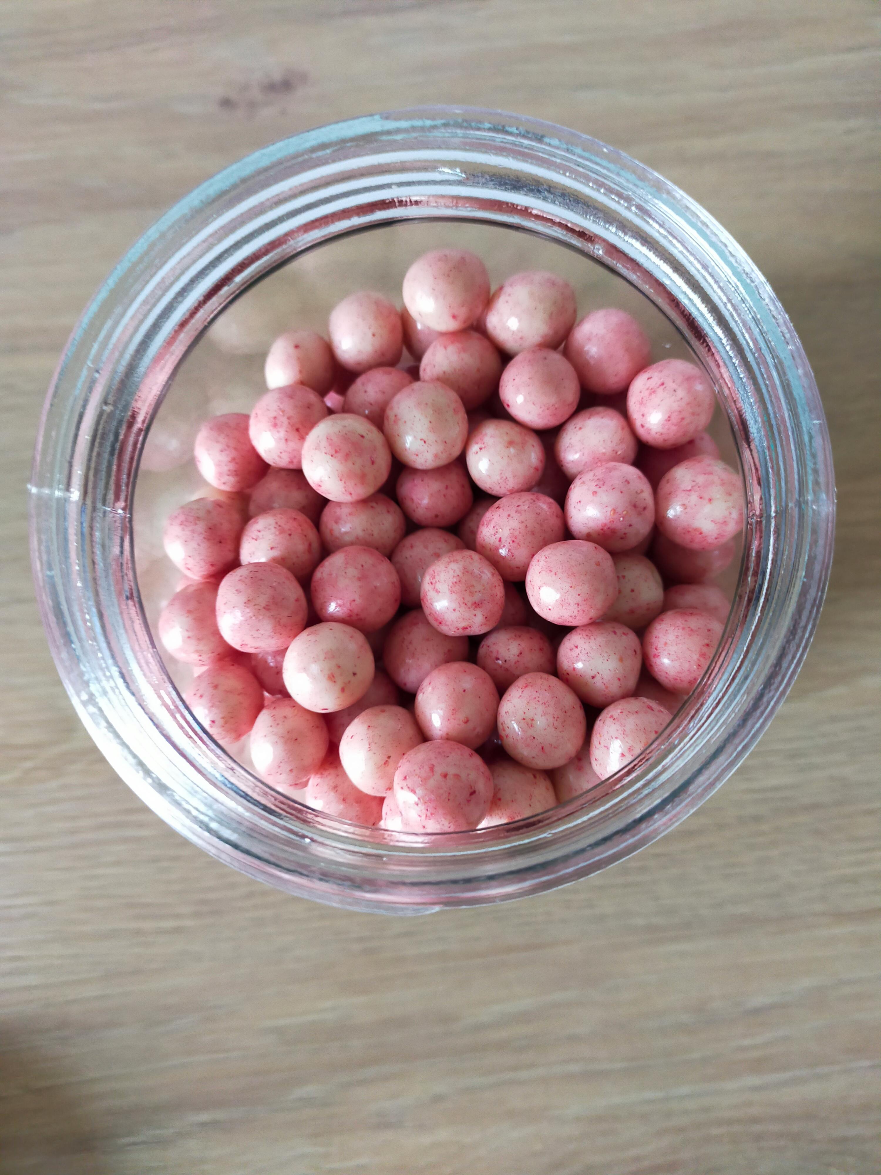 ein glasgefäß gefüllt mit kleinen, runden, rosa bonbons mit roten sprenkeln auf einem holztisch.