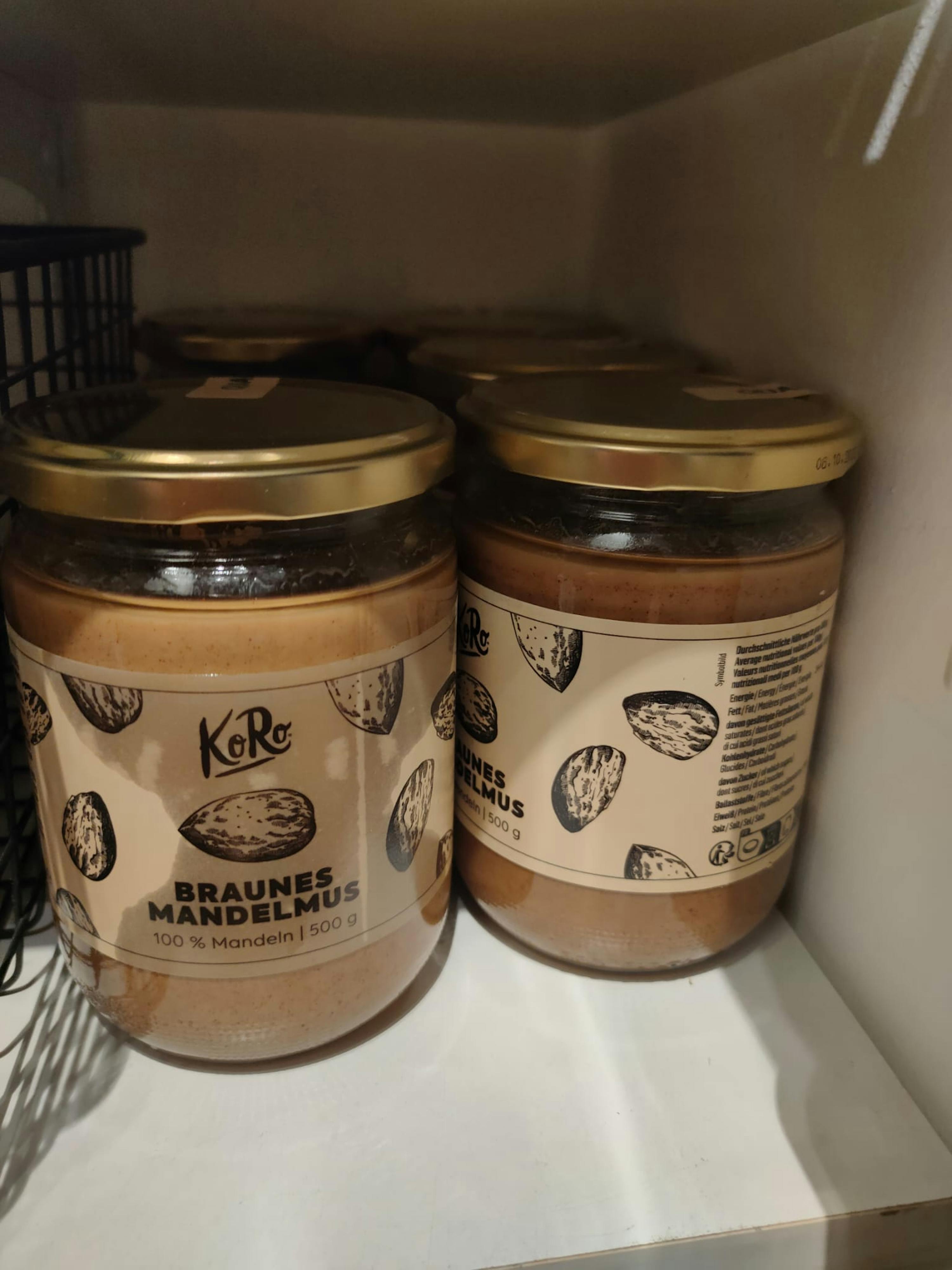 zwei Gläser braunes Mandelmus stehen auf einem Regal