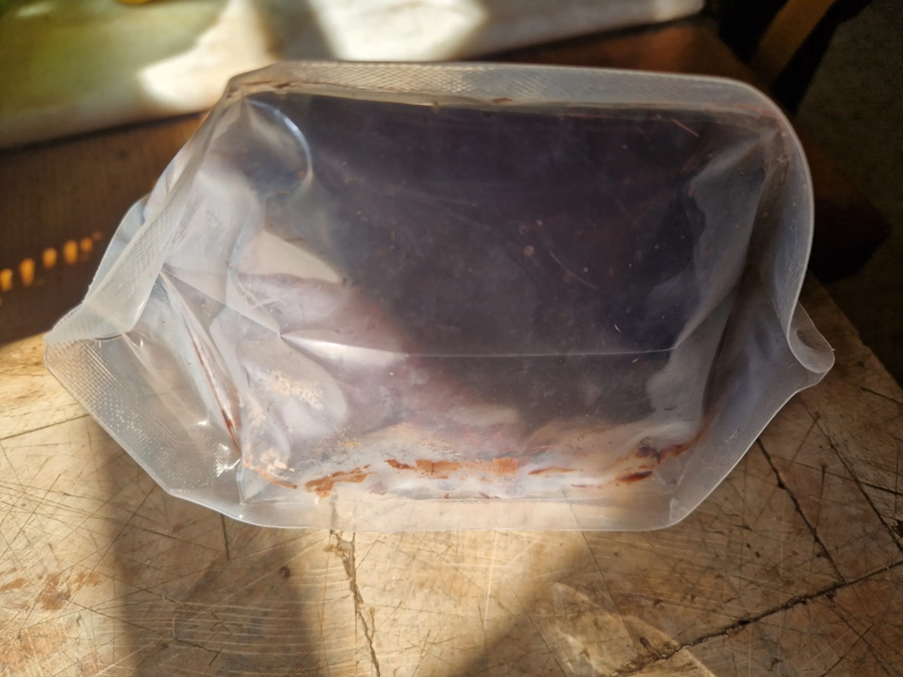 a dark, rectangular item, possibly food, is vacuum-sealed in a clear plastic bag on a wooden surface.