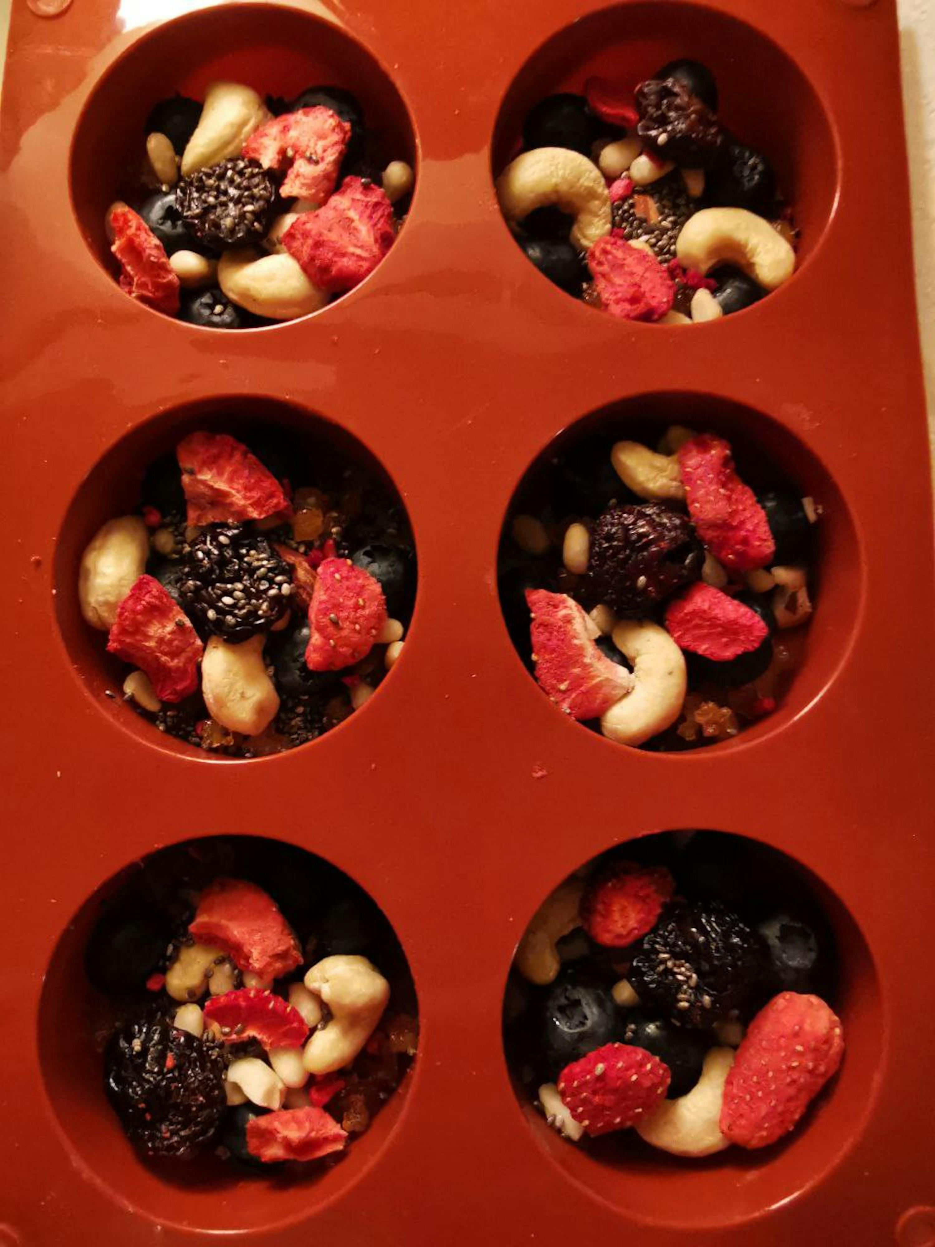 rote silikonform mit sechs mulden, gefüllt mit getrockneten erdbeeren, heidelbeeren, brombeeren, cashewkernen und chiasamen.