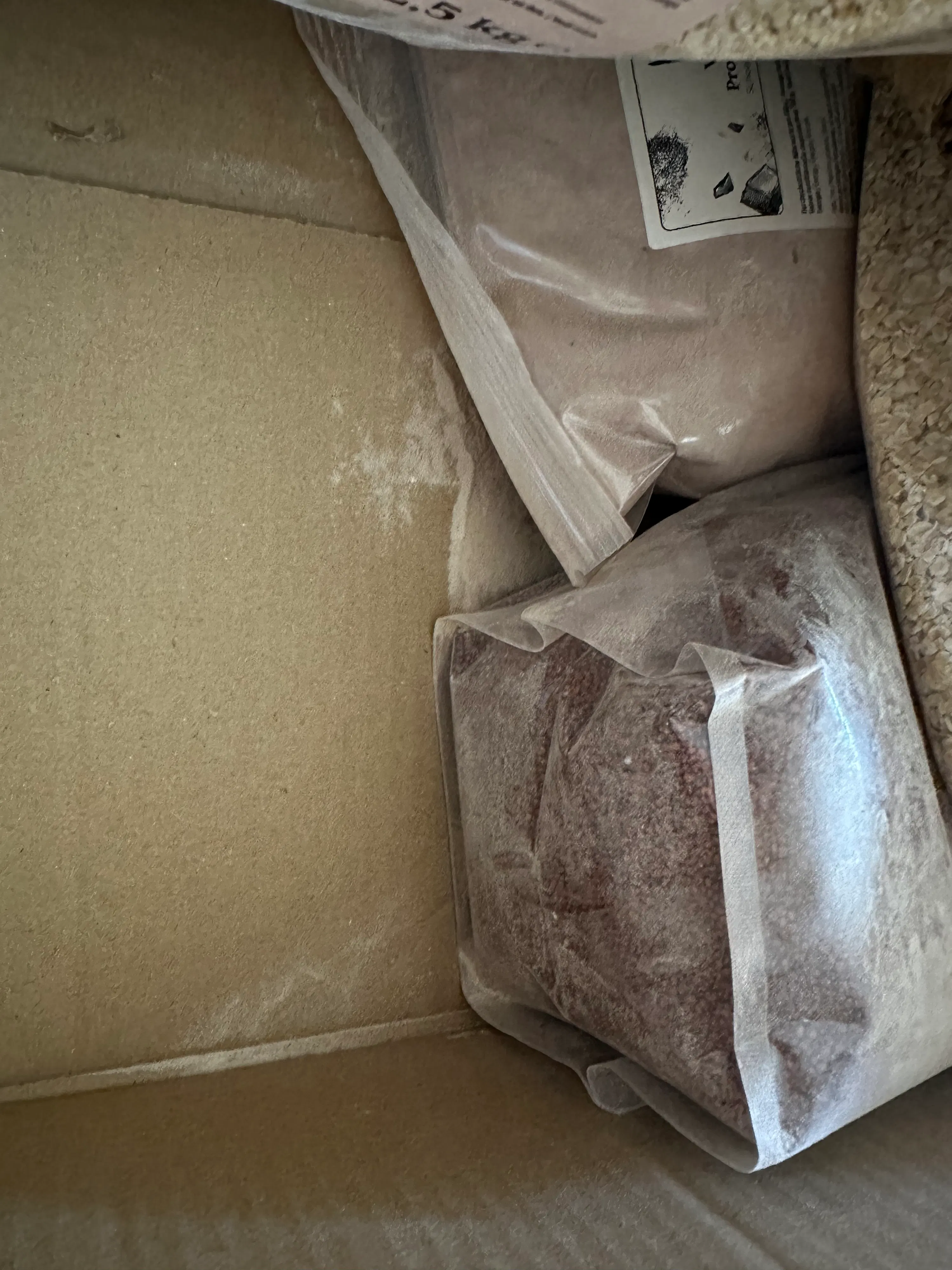 innenansicht eines kartons mit mehreren beuteln trockener lebensmittel und etwas verschüttetem pulver auf dem boden.