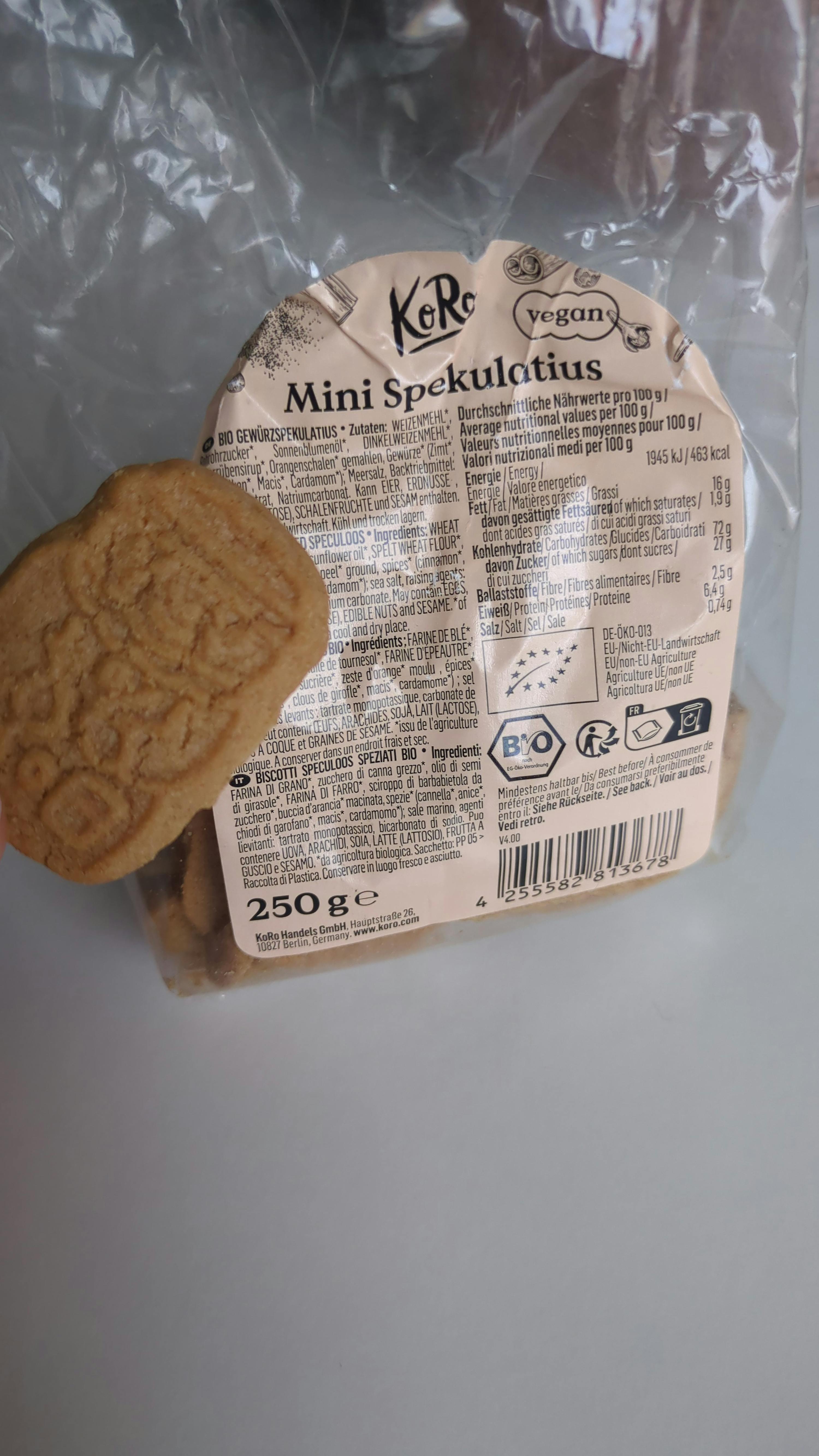 eine durchsichtige plastiktüte mit koro mini spekulatius keksen, wobei ein keks außerhalb der tüte liegt und das vegan- und bio-etikett sichtbar ist.