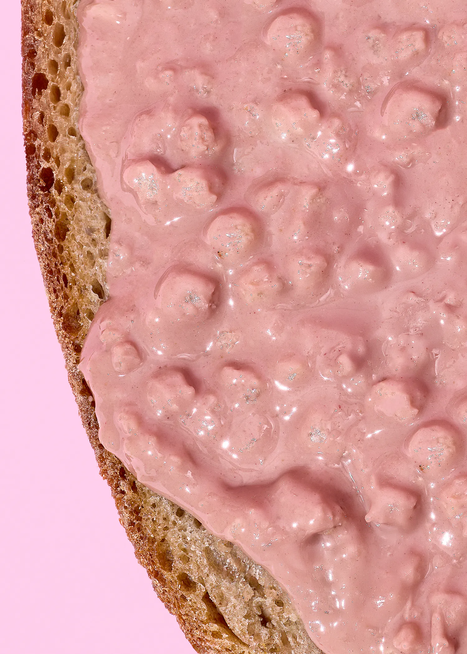 une tranche de pain recouverte d'une pâte rose crémeuse et texturée avec des éclats brillants, sur un fond rose uni.