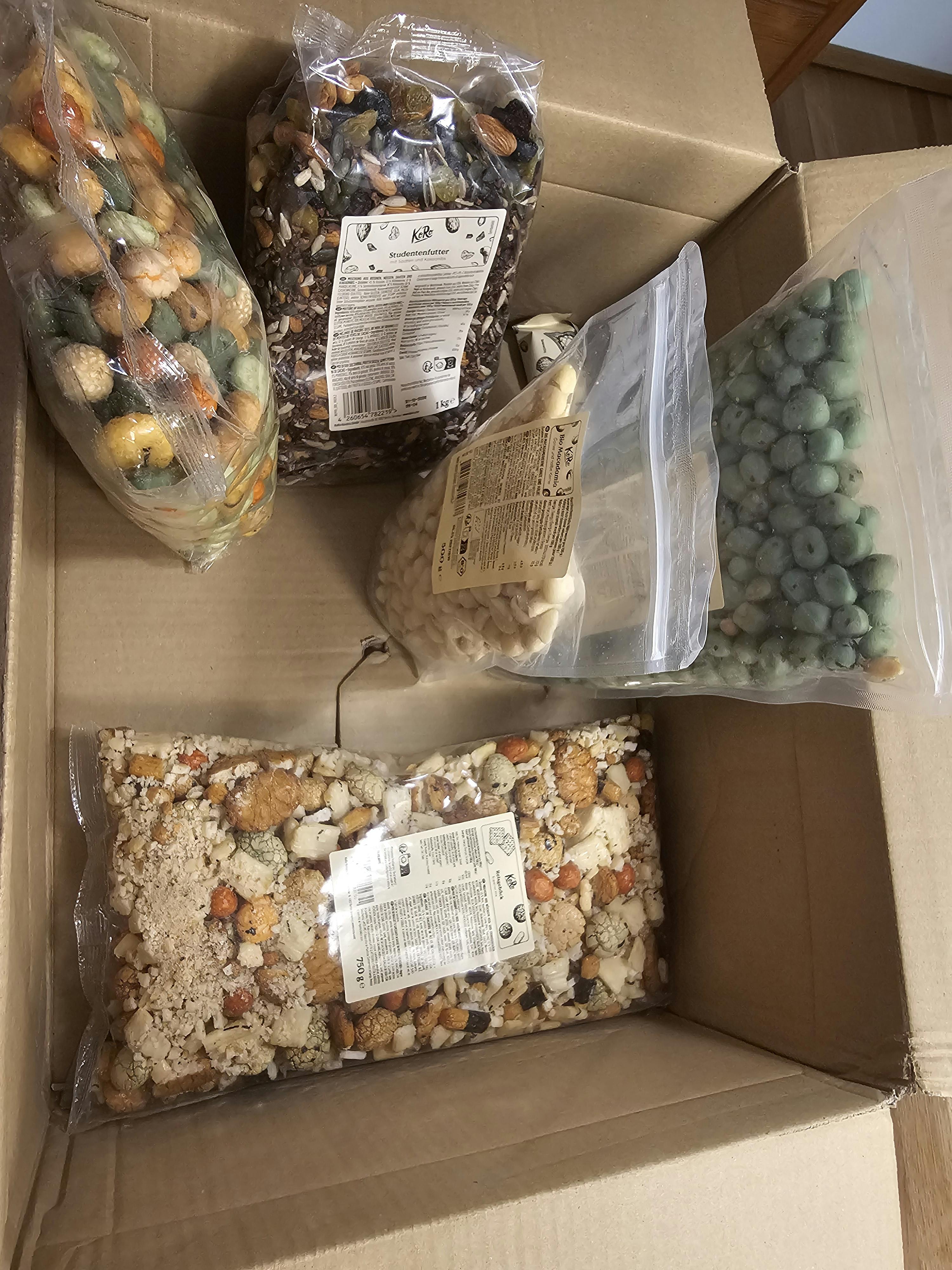 une boîte en carton ouverte remplie de plusieurs sacs transparents contenant diverses collations et noix.