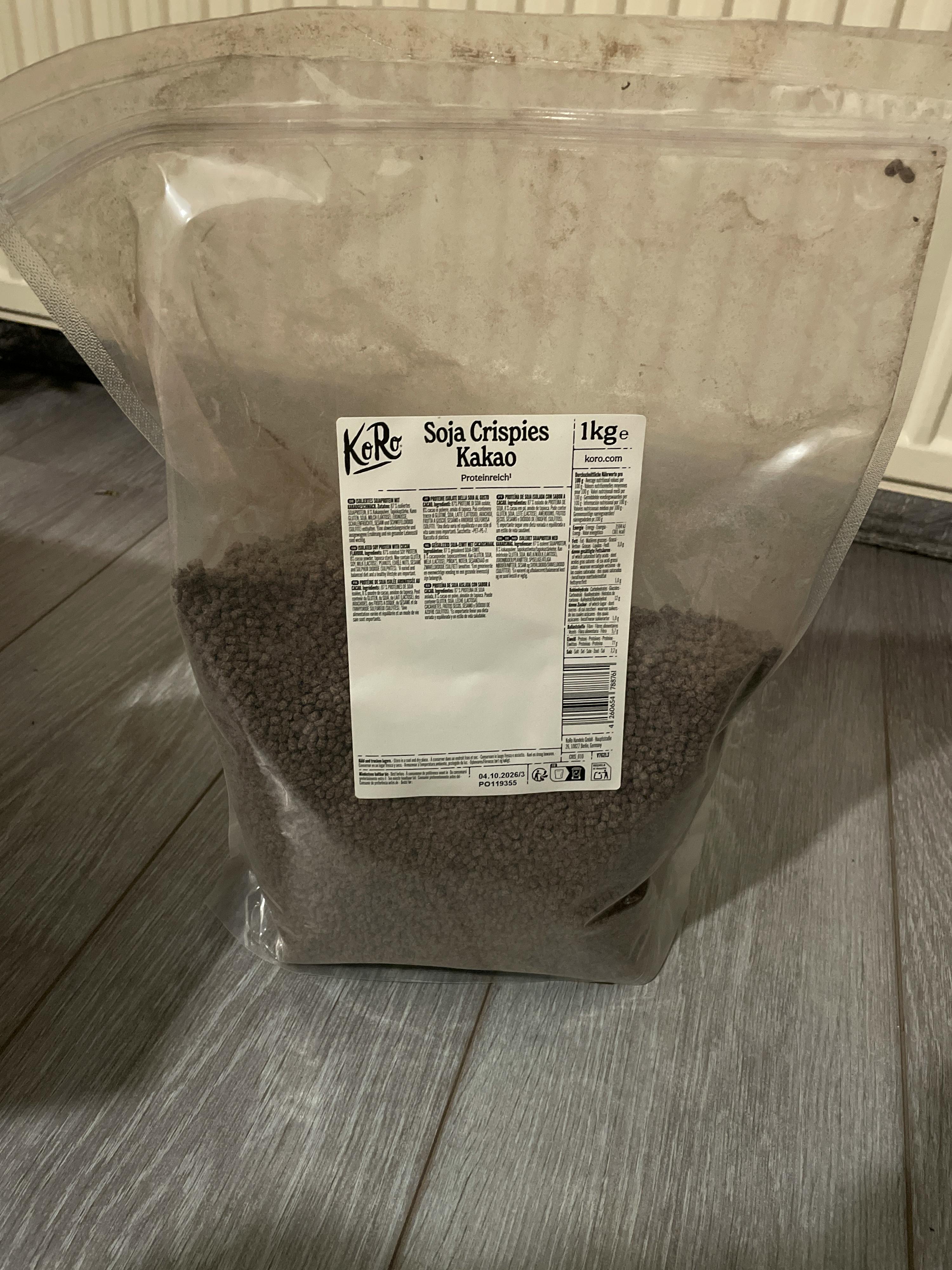 eine transparente plastiktüte mit 1 kg soja crispies kakao, die auf einem holzboden liegt.