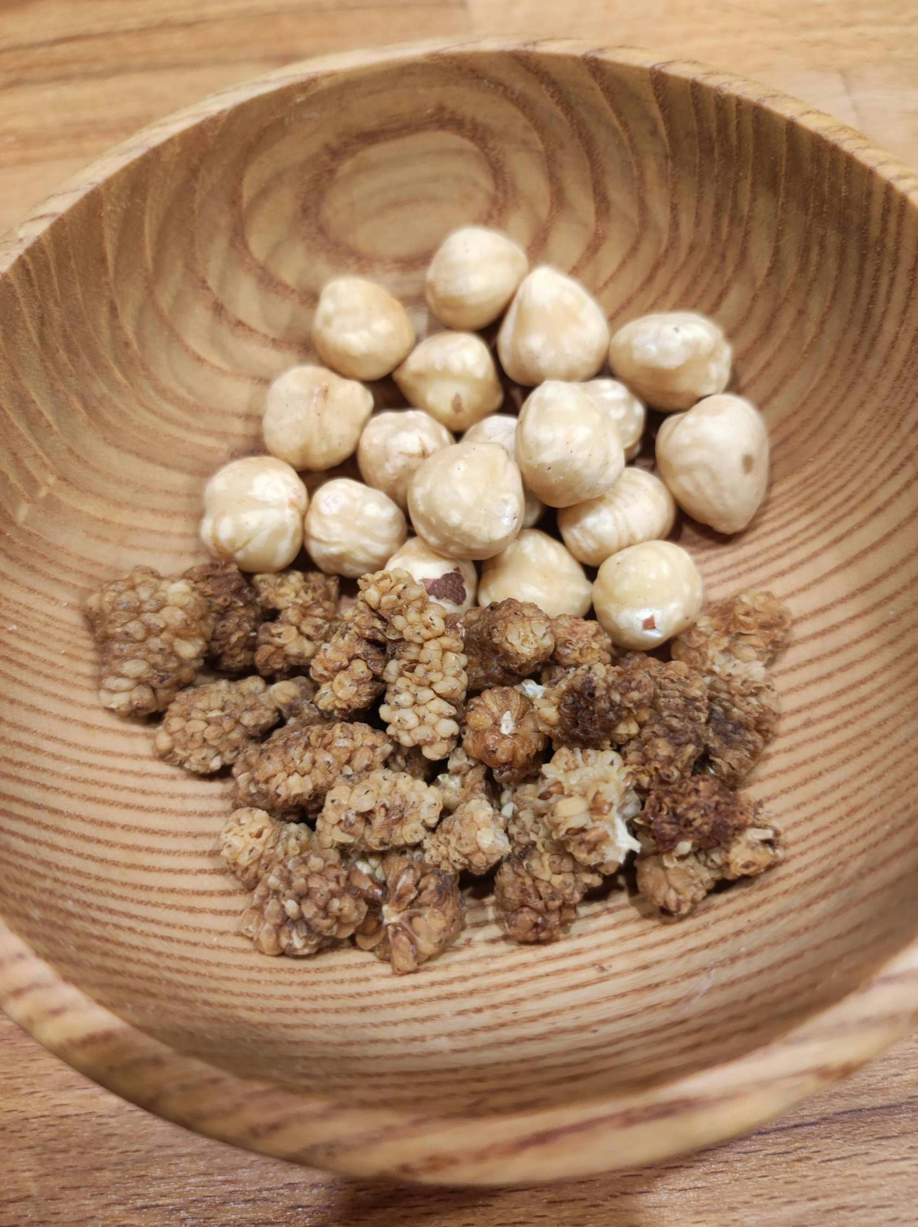 eine Holzschale mit Haselnüssen und Erdnüssen auf einem Holztisch
