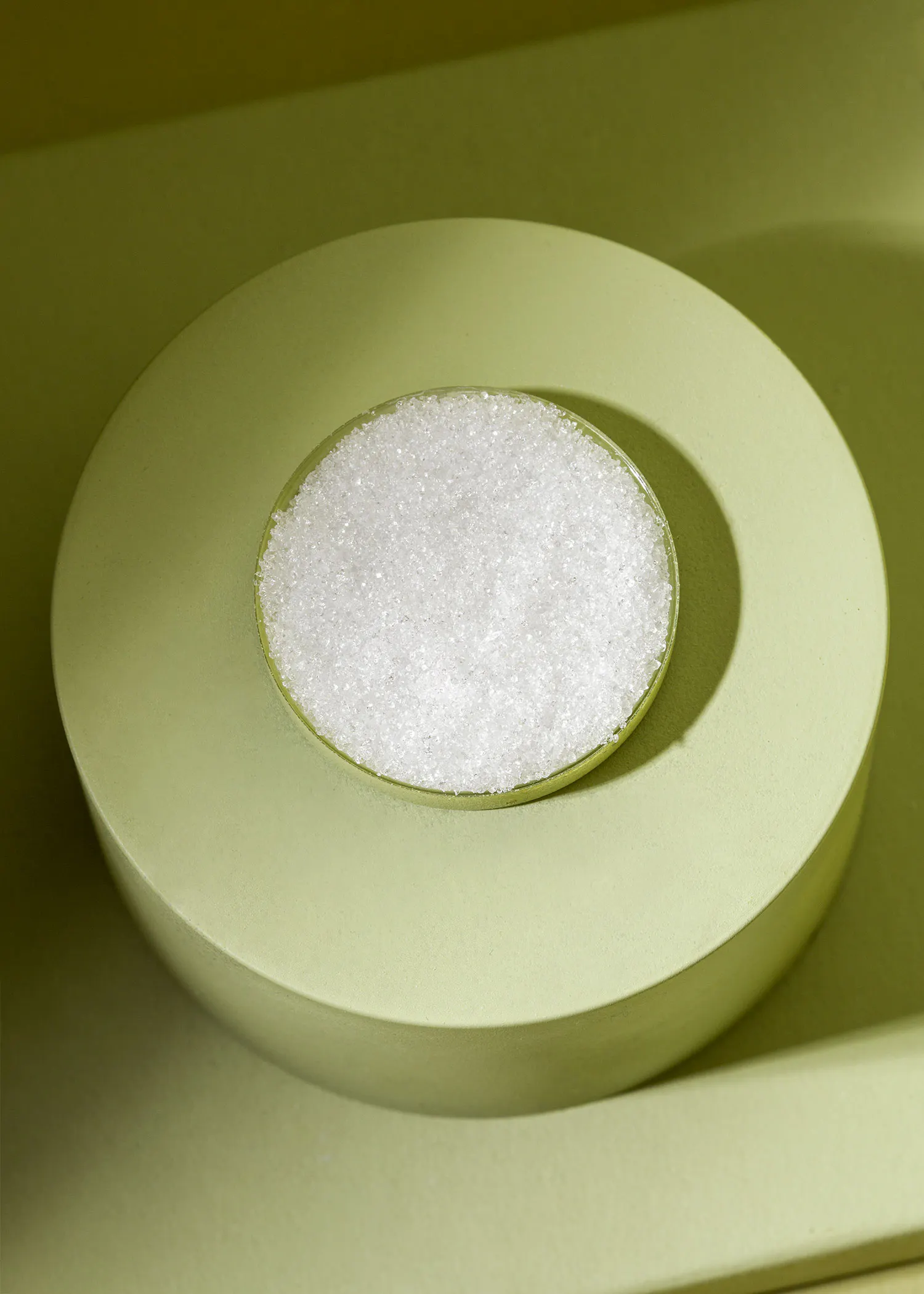 a bowl of white sugar sits on a green surface