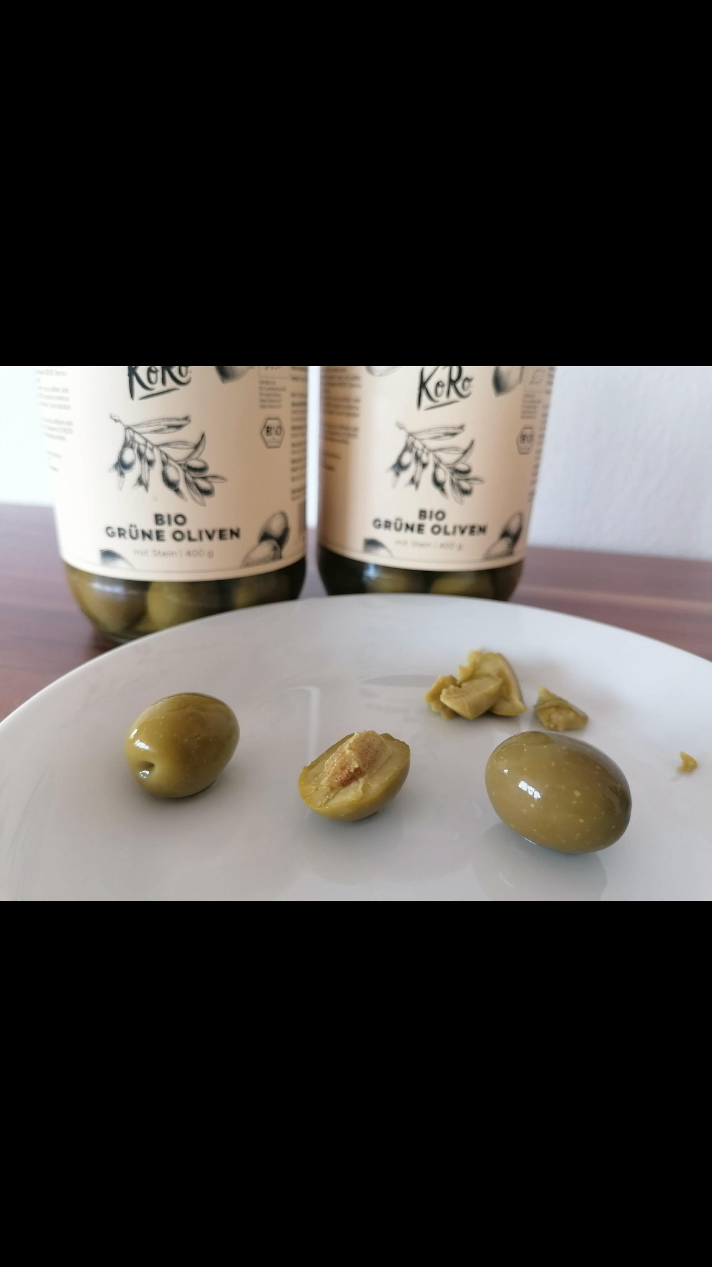 two bottles of green olives next to a plate of olives