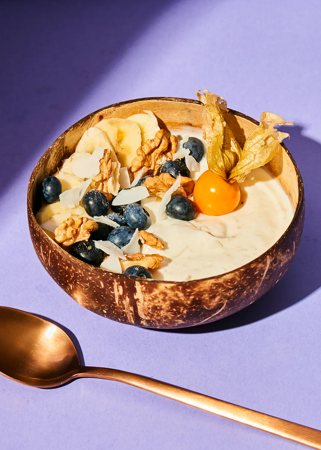 un bol de yogourt avec des bleuets et des noix de coco et une cuillère à côté
