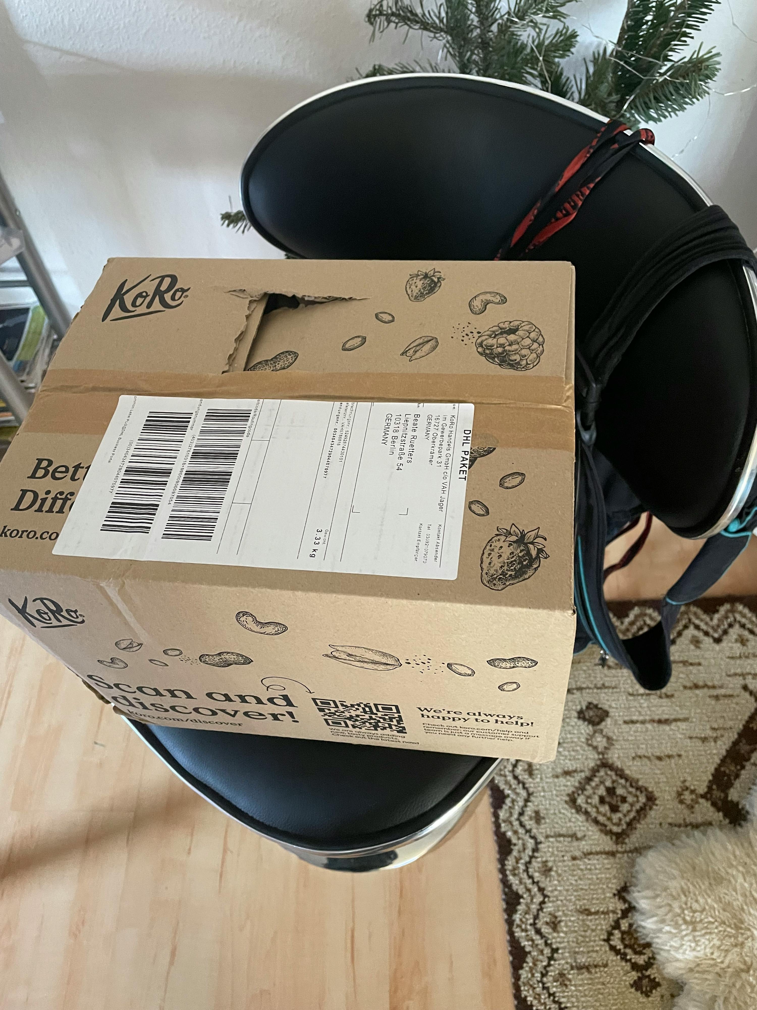 una scatola di cartone dhl con etichetta di spedizione e illustrazioni di frutta e noci, appoggiata su una sedia nera.