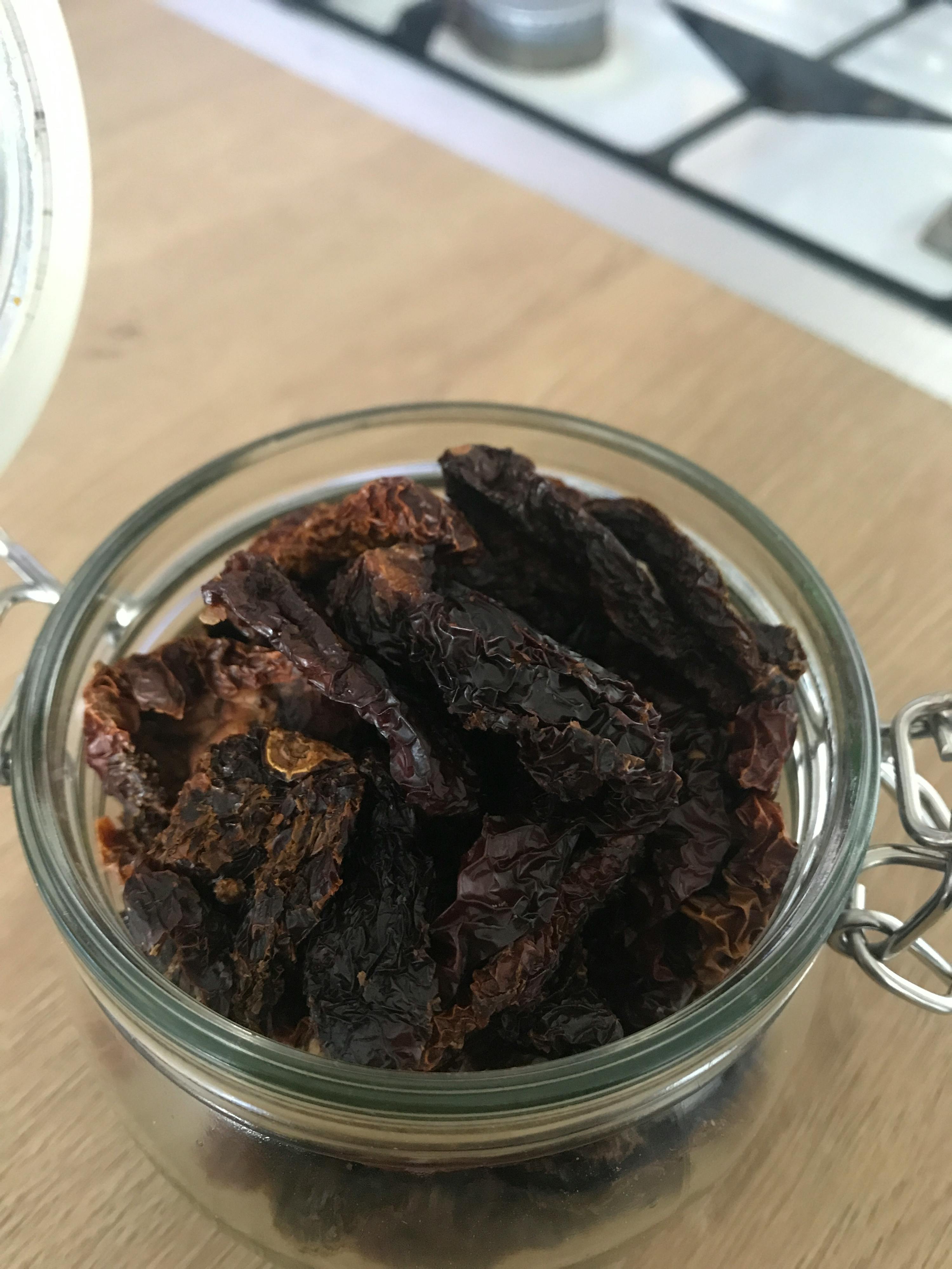 a glass jar filled with dried tomatoes on a table