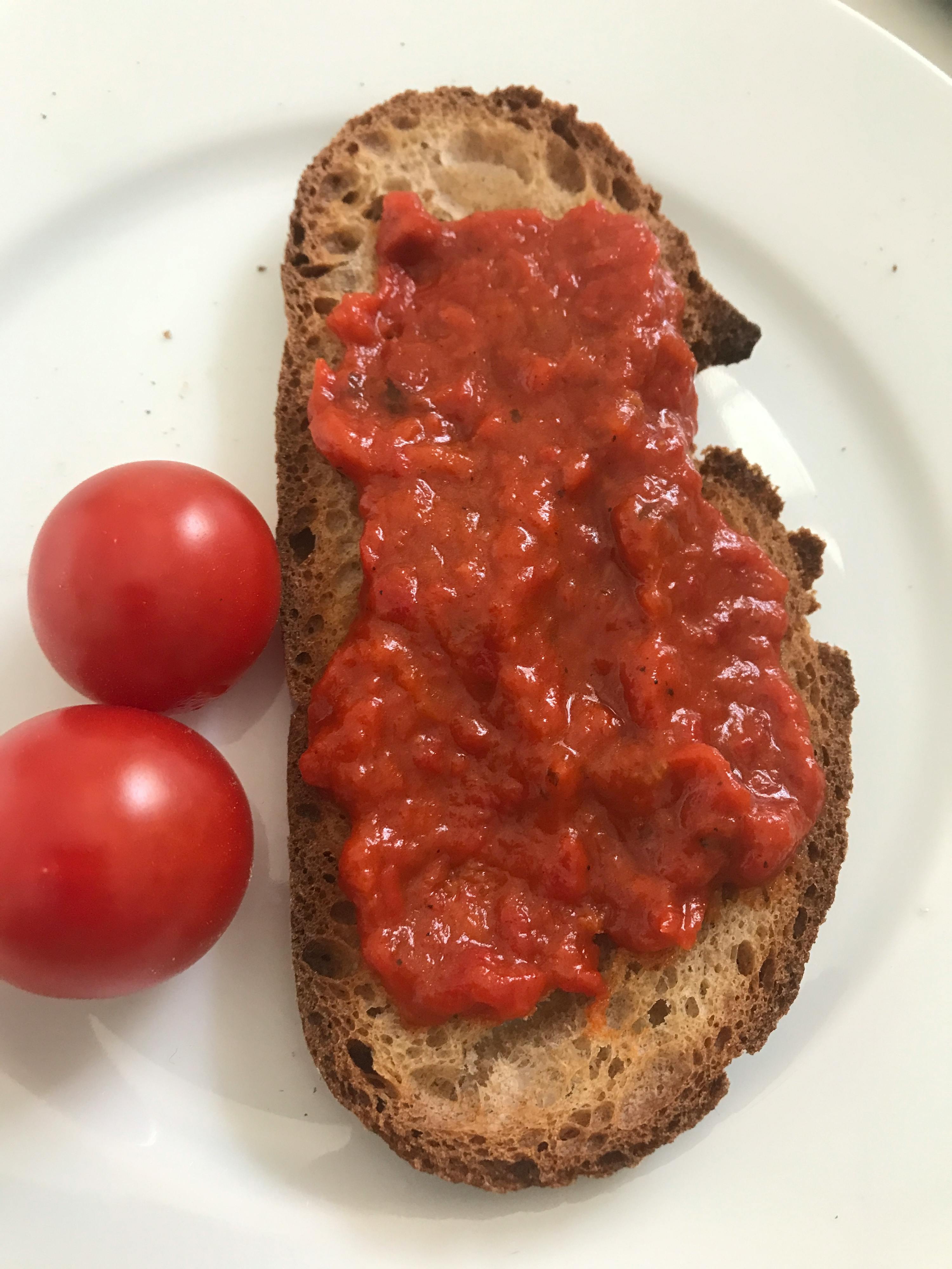 ein Stück Brot mit Tomatensauce und zwei Tomaten auf einem Teller