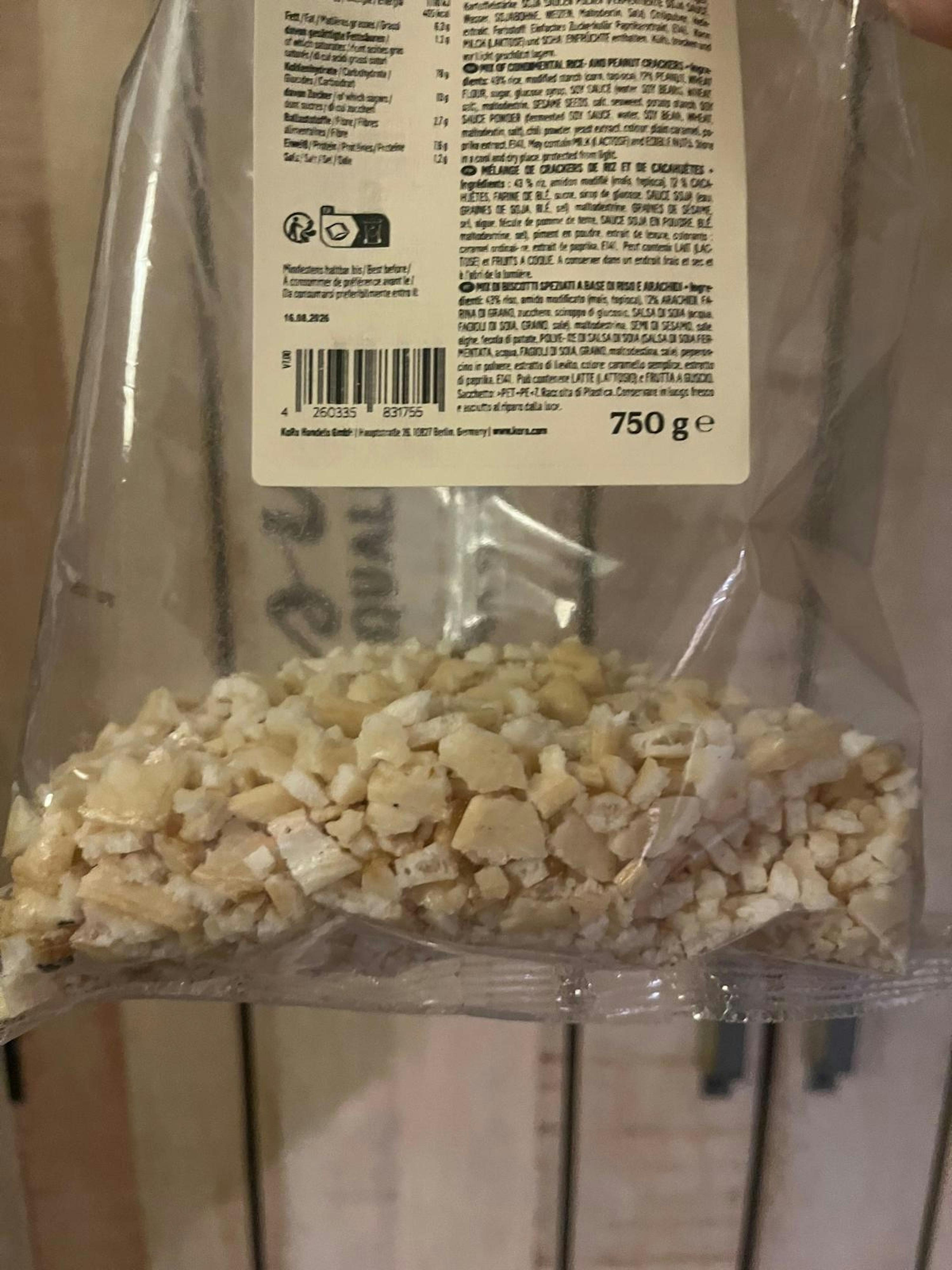 un sac en plastique transparent rempli de petits morceaux de crackers ou de cacahuètes, avec des informations sur le produit, un code-barres et l'indication 750 ge visibles sur l'emballage.