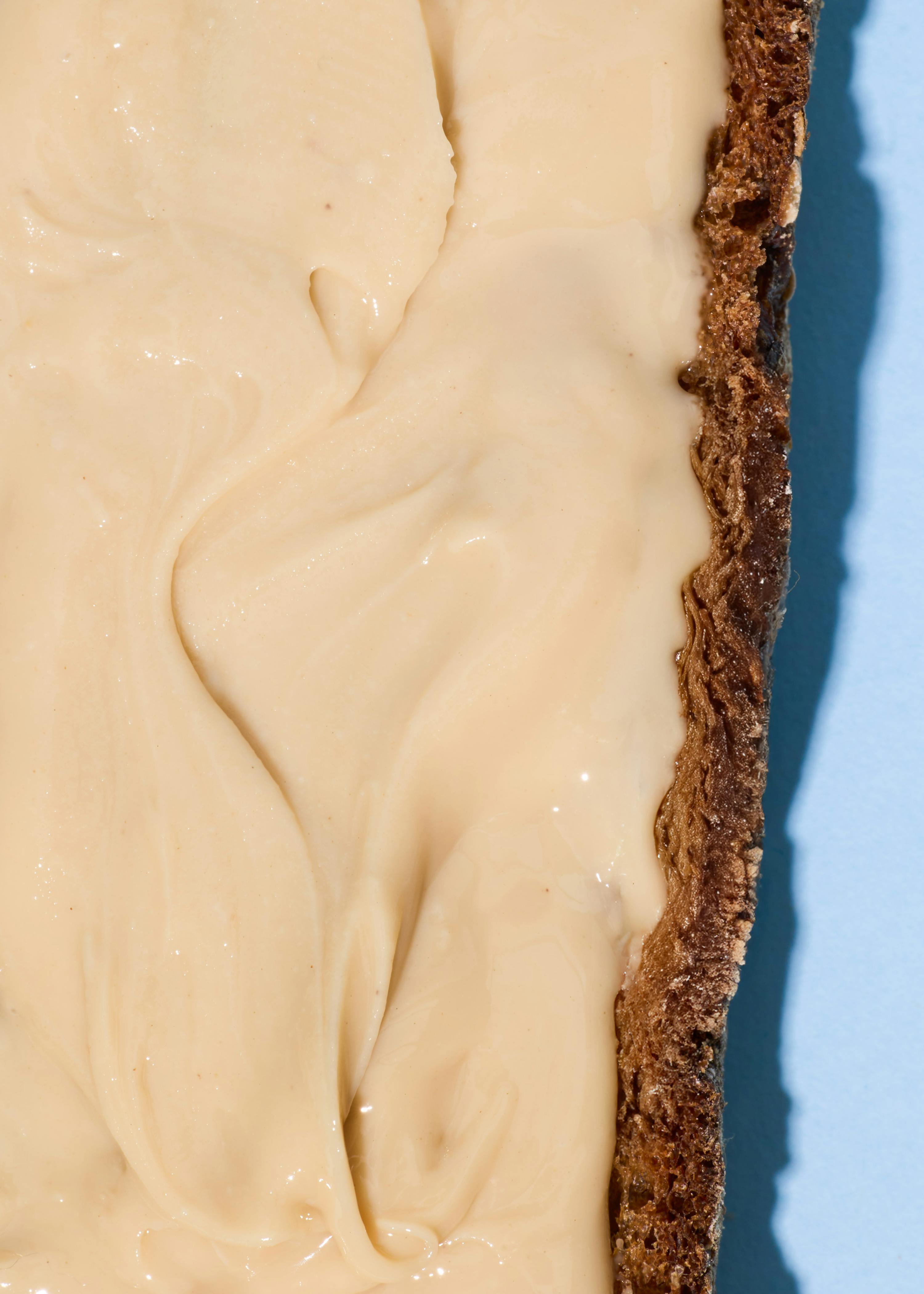 eine nahaufnahme einer hellen, cremigen masse mit sanften wirbeln, die einen dunklen, strukturierten rand bedeckt, vor einem hellblauen hintergrund.