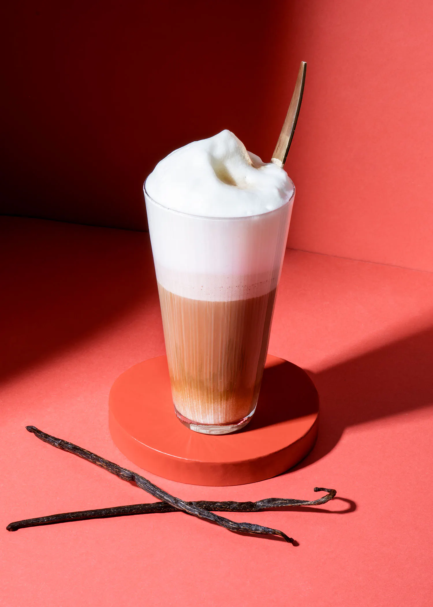 deux bâtons de vanille sont assis à côté d' un verre de cappuccino