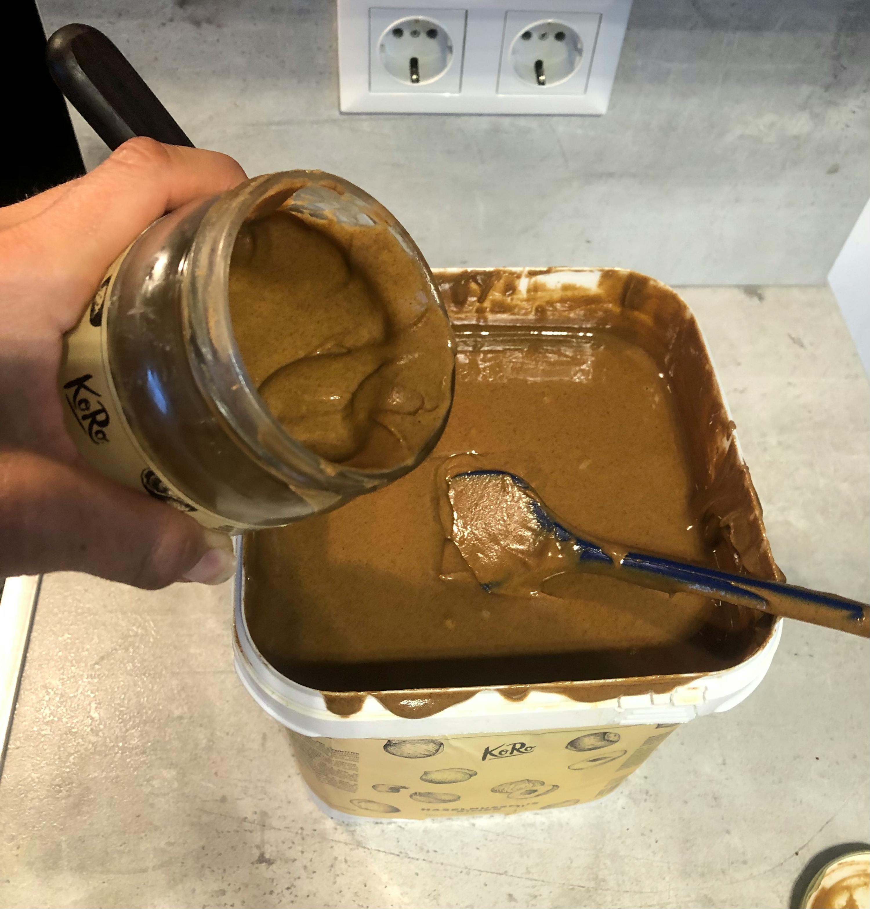 eine Person gießt Erdnussbutter in einen Eimer mit einem Löffel