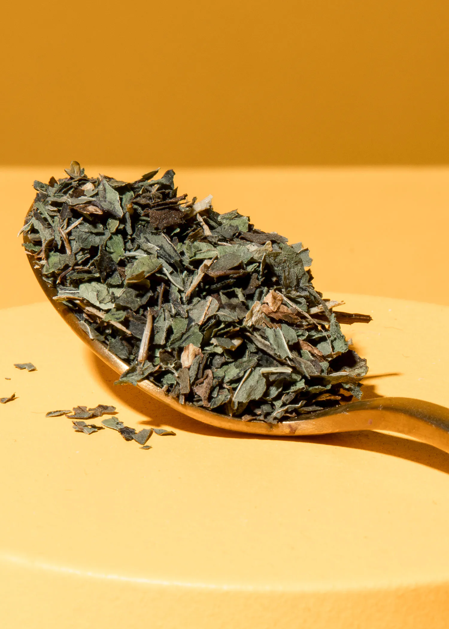 ein Löffel gefüllt mit grünem Tee liegt auf einem gelben Tisch