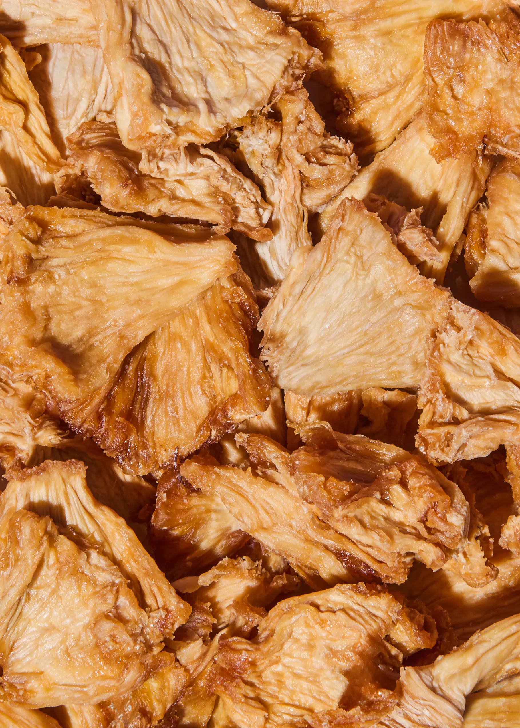 a close-up view of many irregularly shaped, golden-brown dried pineapple pieces.