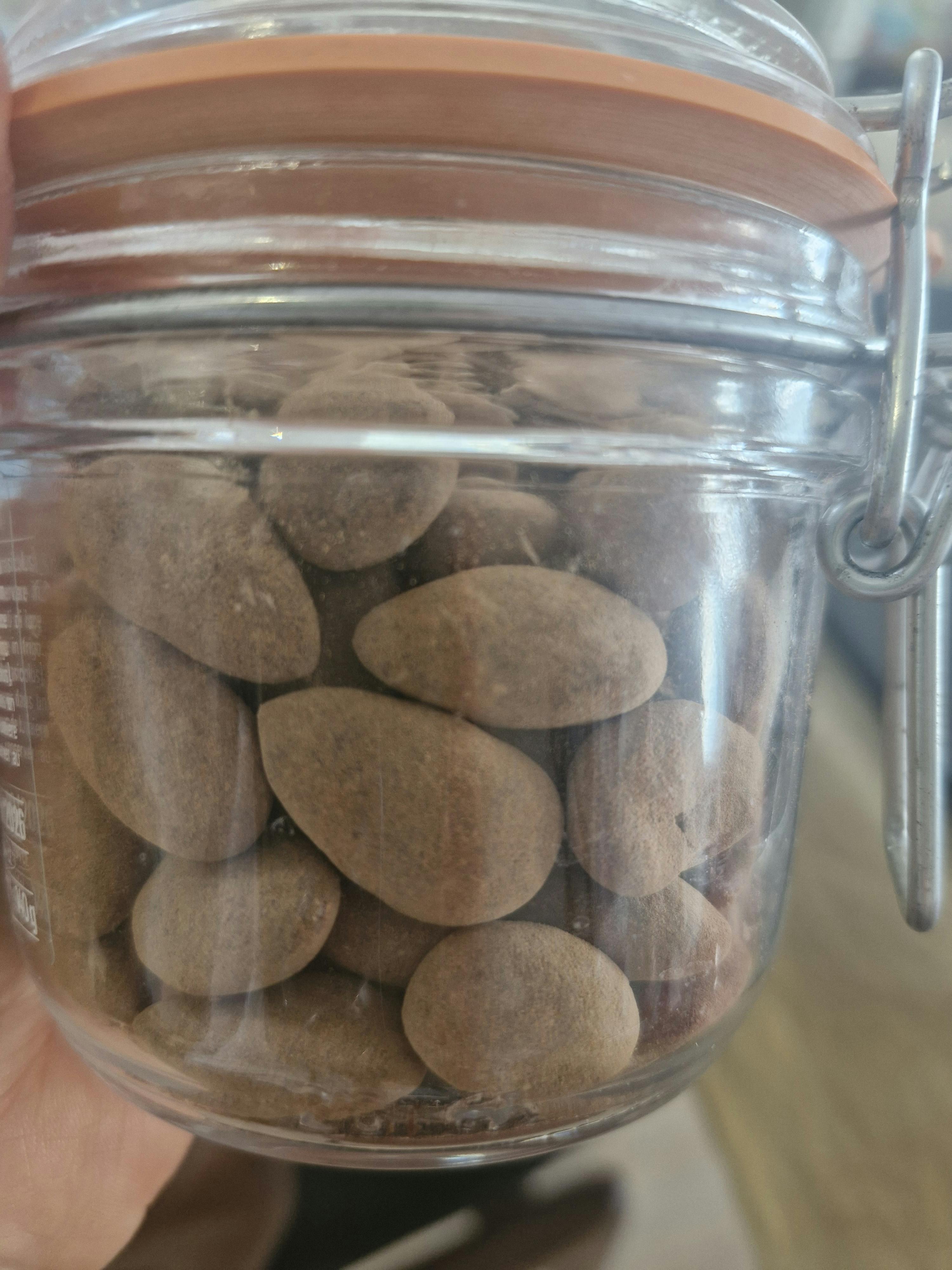 ein klares glasgefäß, gefüllt mit braunen, kieselsteinartigen bonbons, wird von einer hand gehalten.