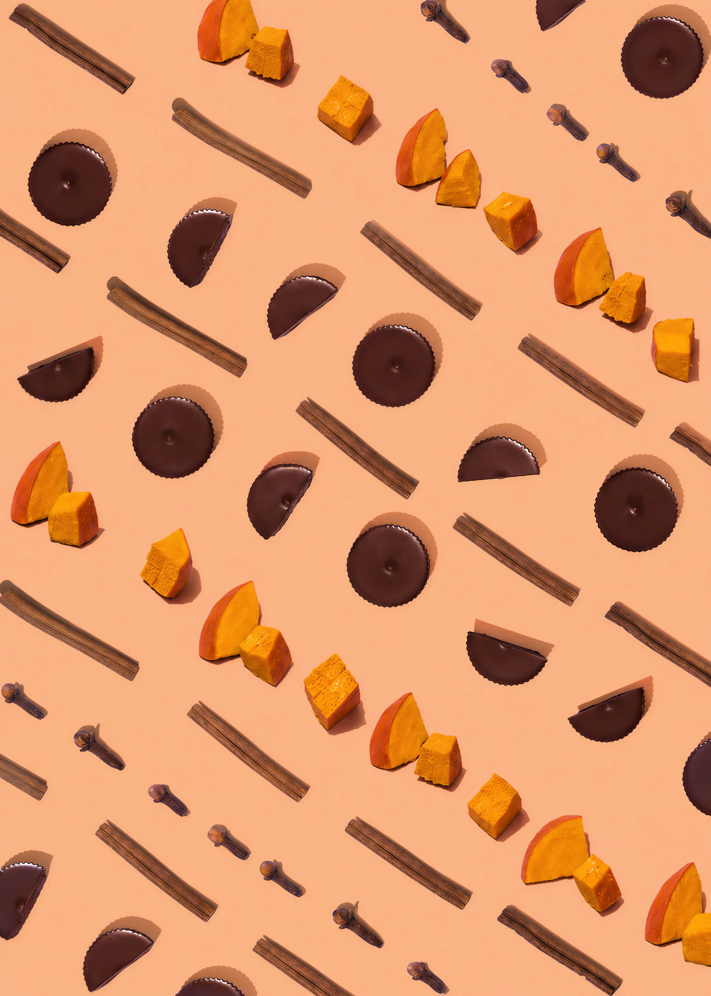 composizione ordinata di pezzi di zucca, bastoncini di cannella, chiodi di garofano e cioccolatini su sfondo color pesca.