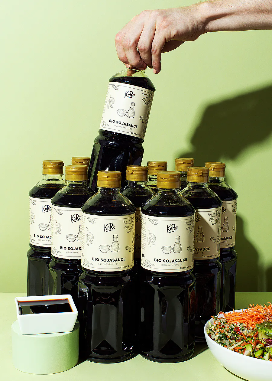 eine Person stapelt eine Flasche bio sojasauce auf einer anderen Flasche