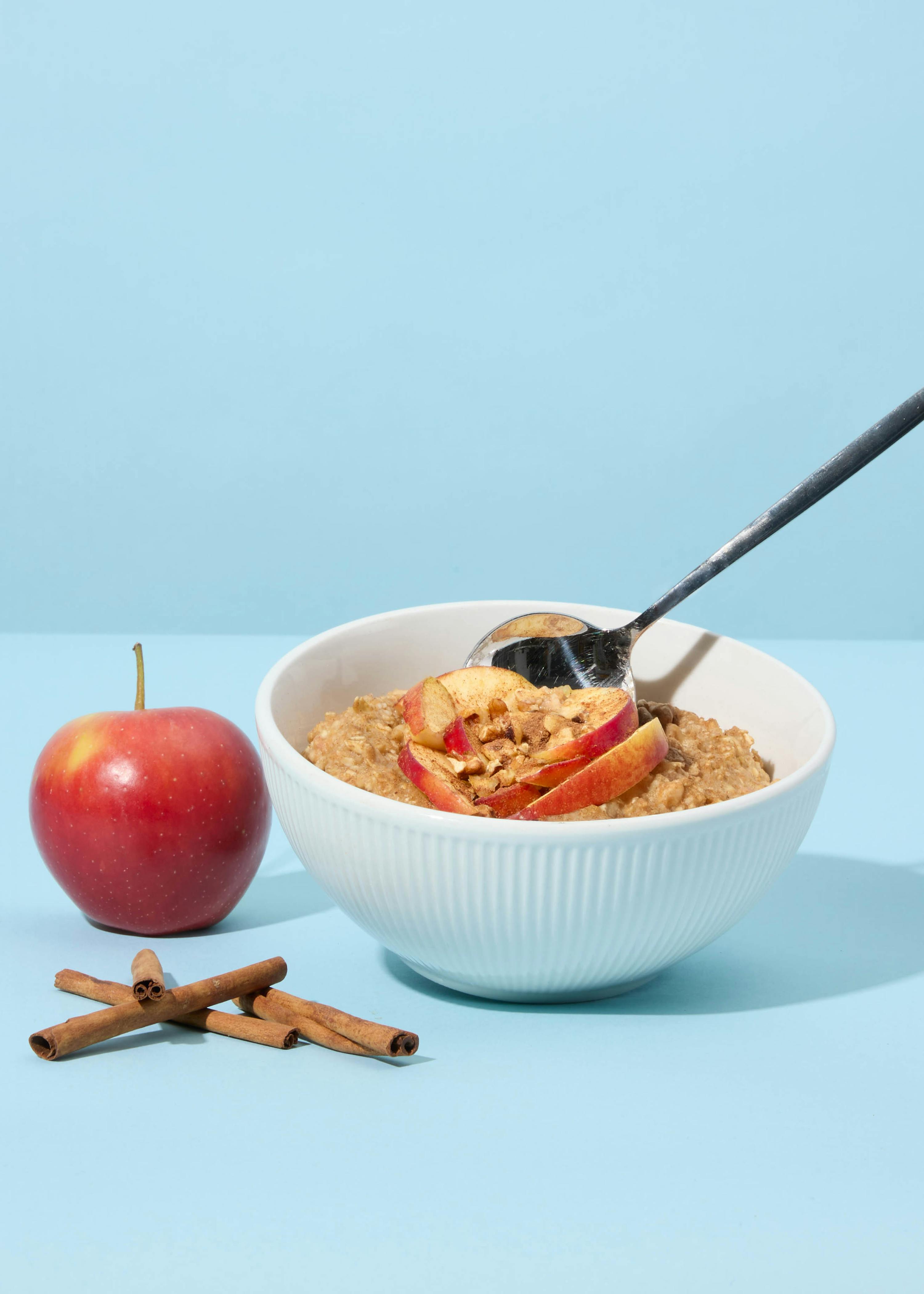 una ciotola di avena con mele e cannella accanto a una mela
