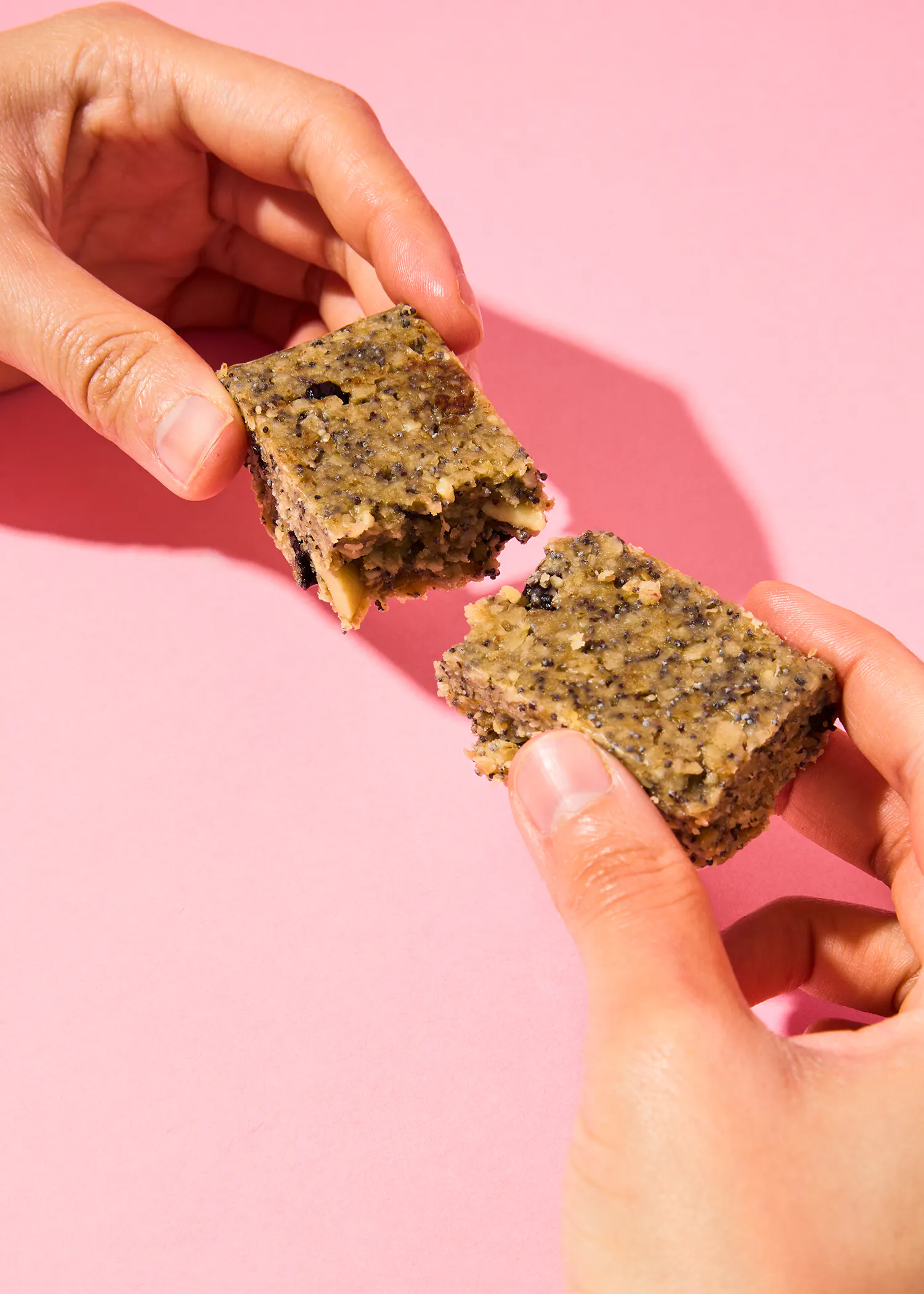 deux mains tenant un morceau de nourriture sur un fond rose