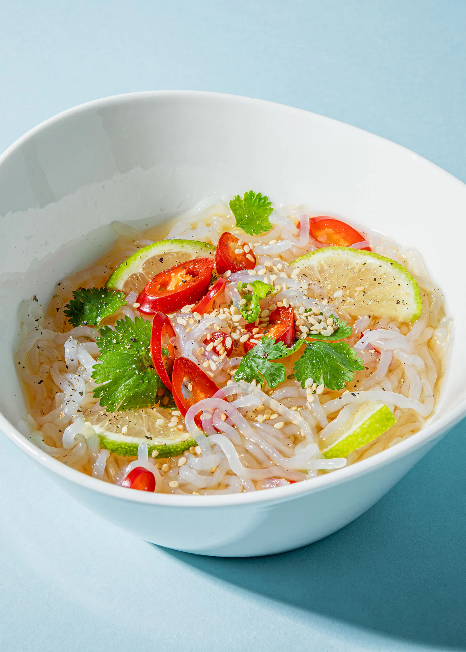 eine weiße Schüssel mit Nudeln und Gemüse auf blauem Hintergrund
