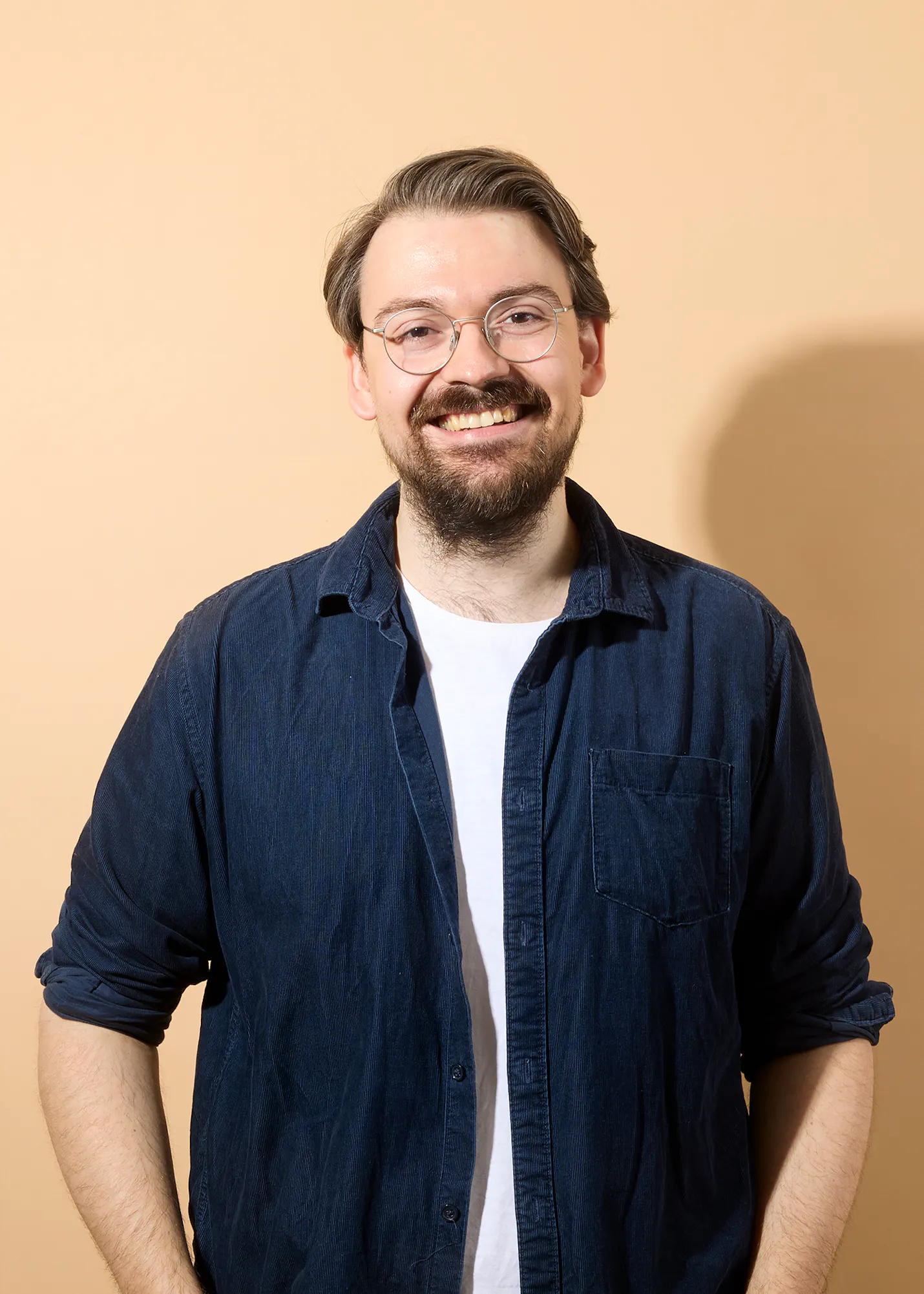 un homme avec une barbe et des lunettes sourit à la caméra