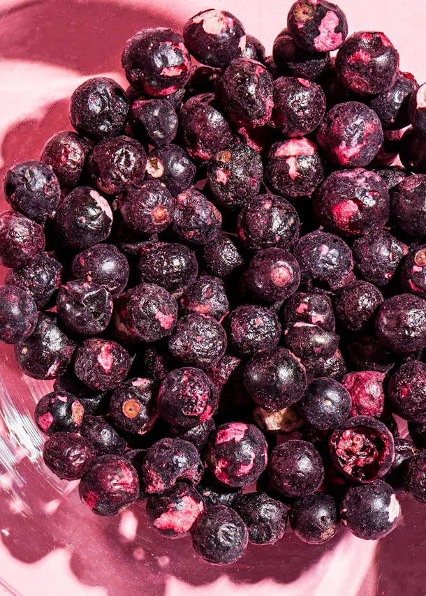 a bowl of frozen blueberries on a pink surface