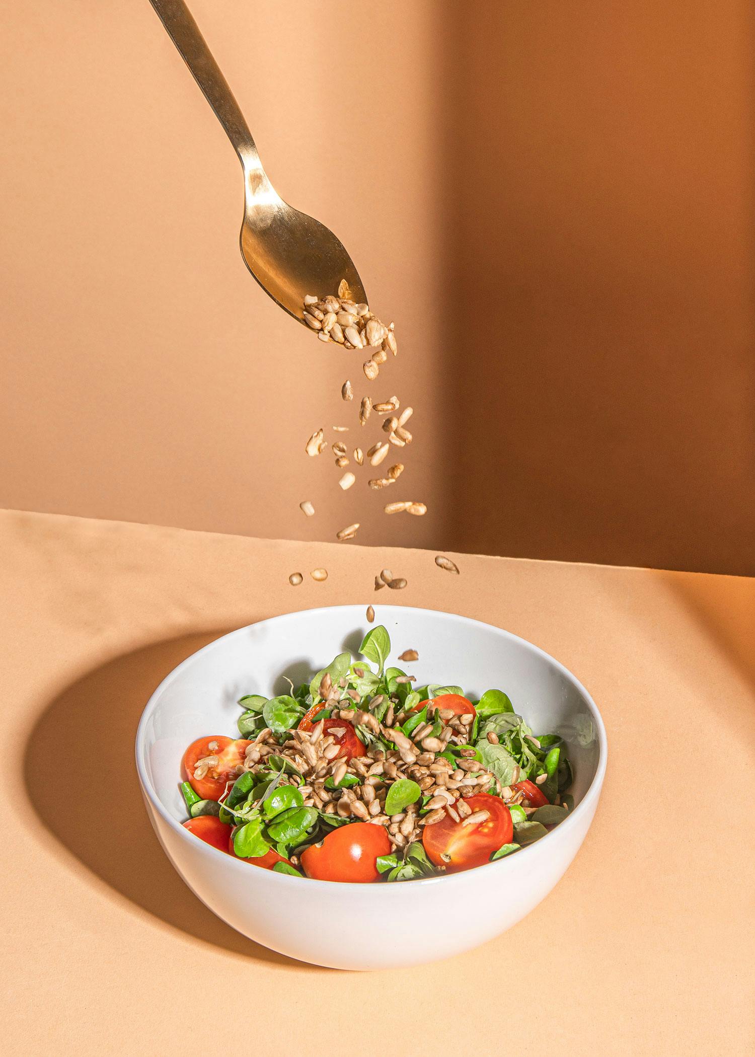 a bowl of salad with tomatoes and seeds being poured into it