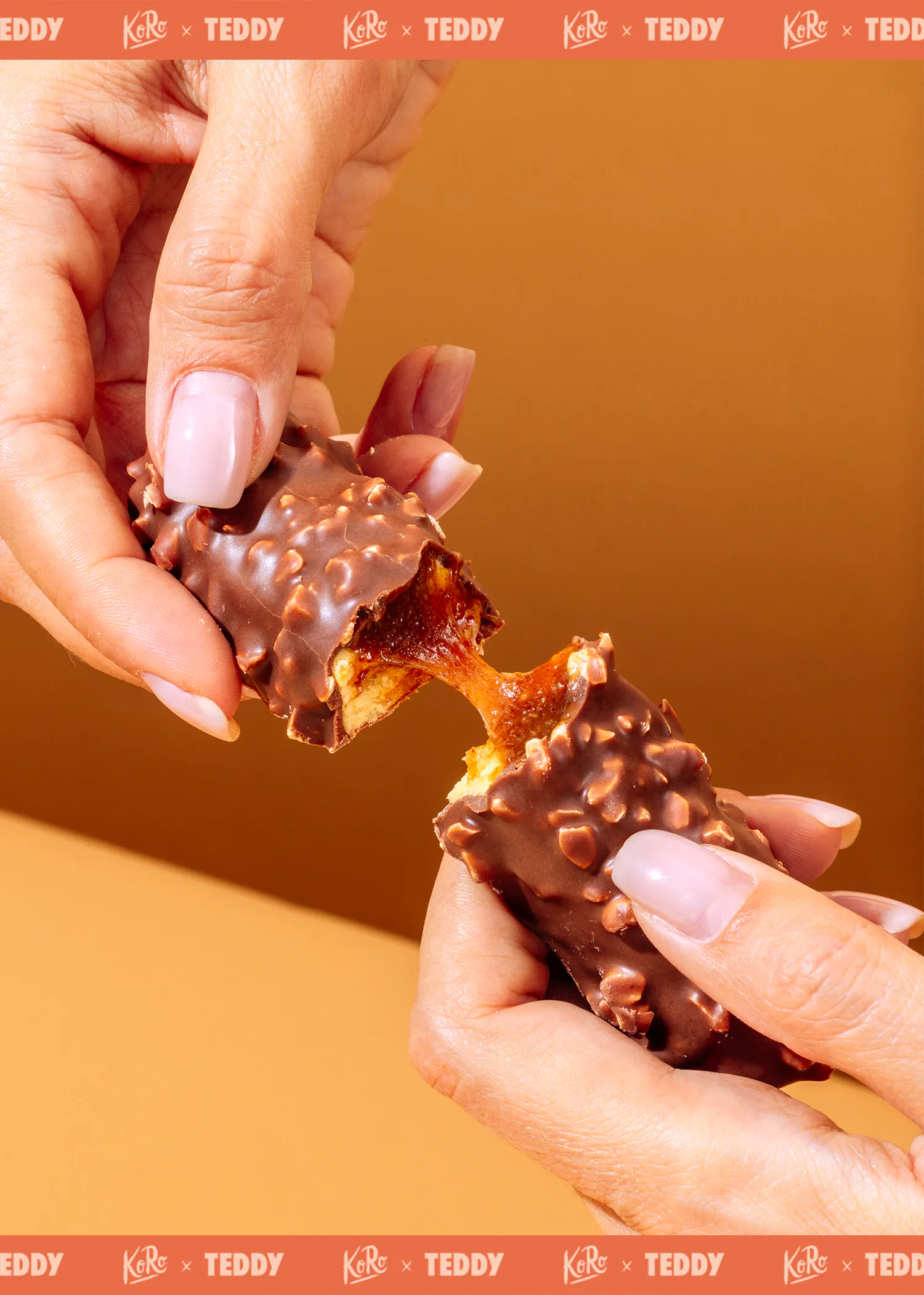 deux mains cassent une barre chocolatée recouverte de noix, révélant un cœur de caramel coulant et doré.