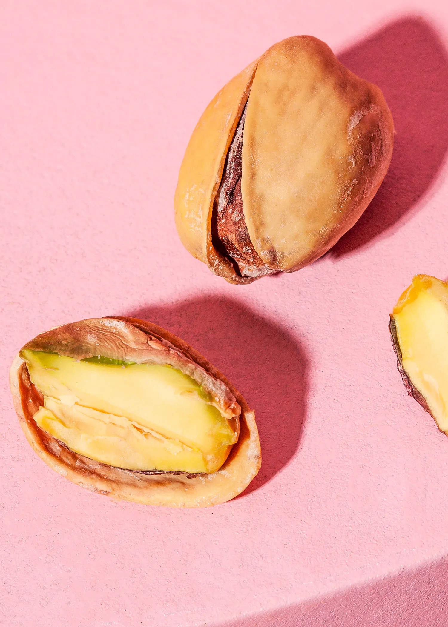 zwei Pistazien auf einem rosa Hintergrund mit einer halbierten Pistazien