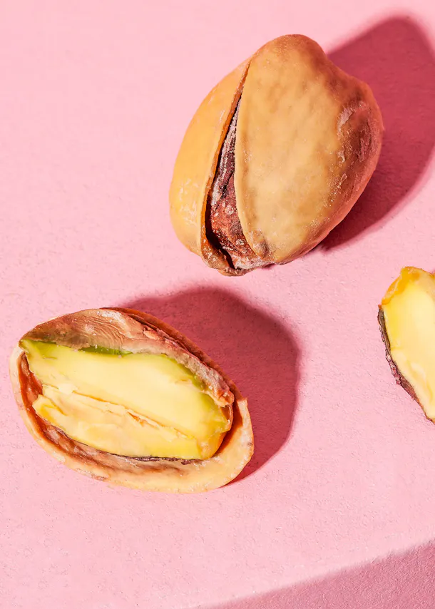 zwei Pistazien auf einem rosa Hintergrund mit einer halbierten Pistazien