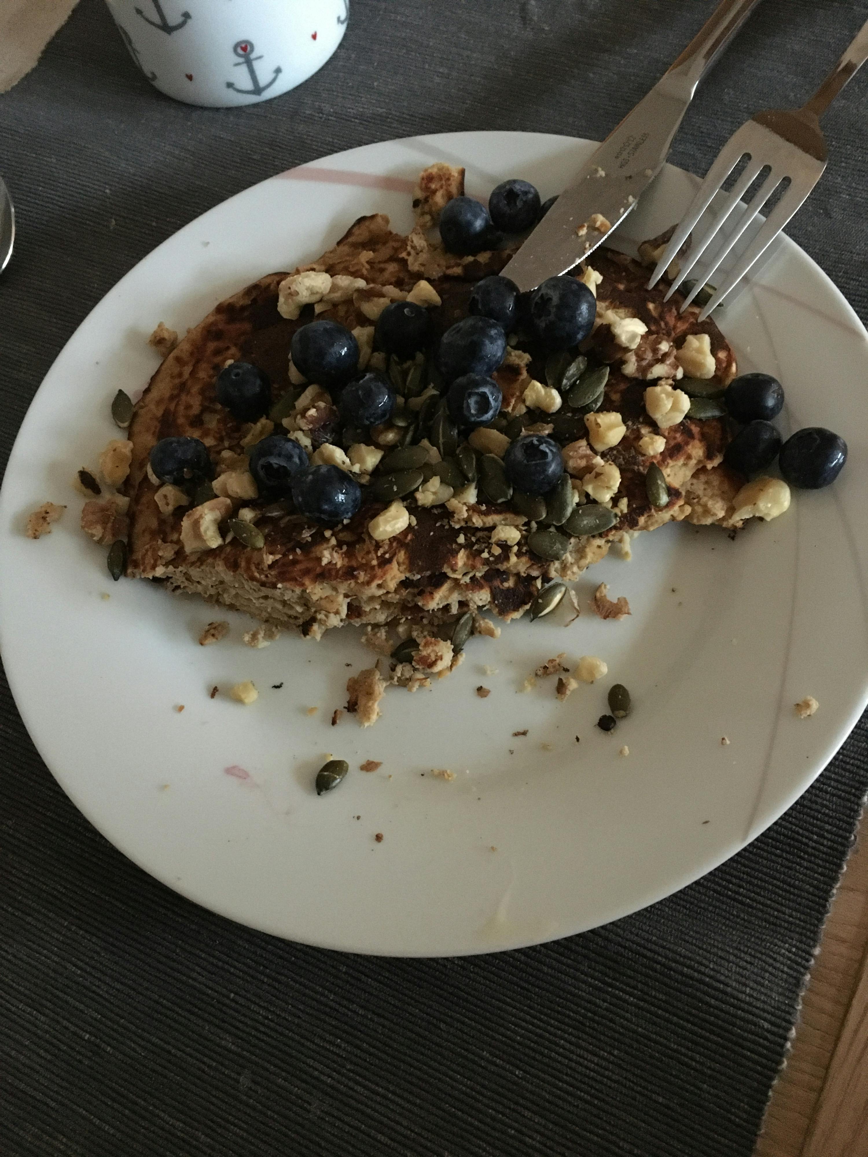 ein weißer Teller mit einem Stück Essen mit Blaubeeren und Nüssen darauf