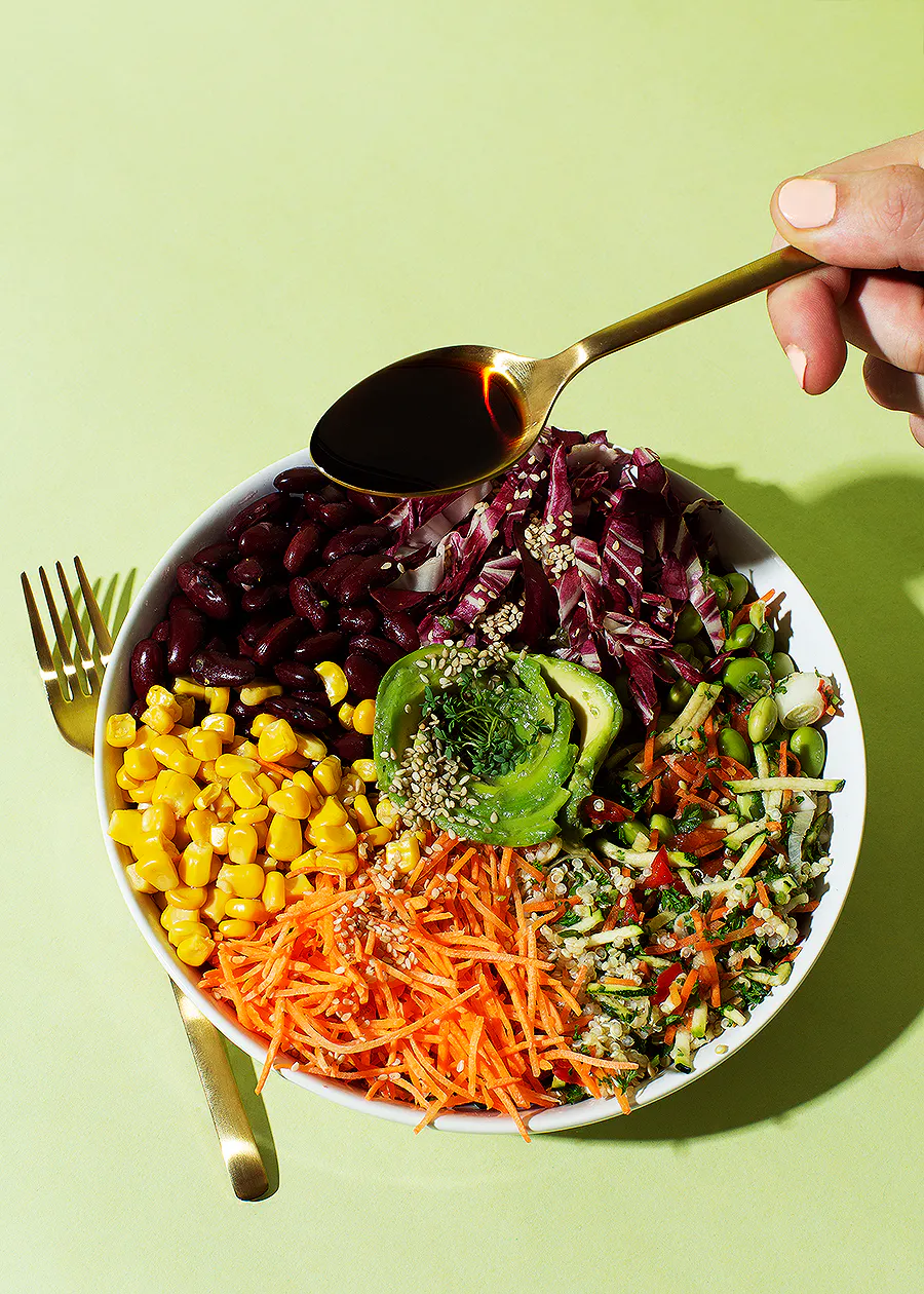 Eine Person gießt einen Salat mit einem Löffel Soße