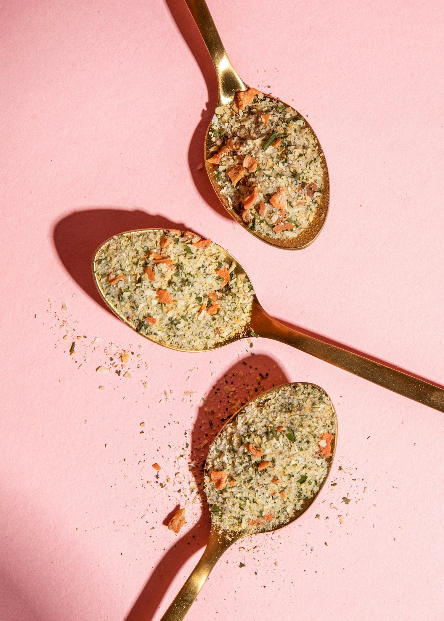 tre cucchiai pieni di spezie su un tavolo rosa