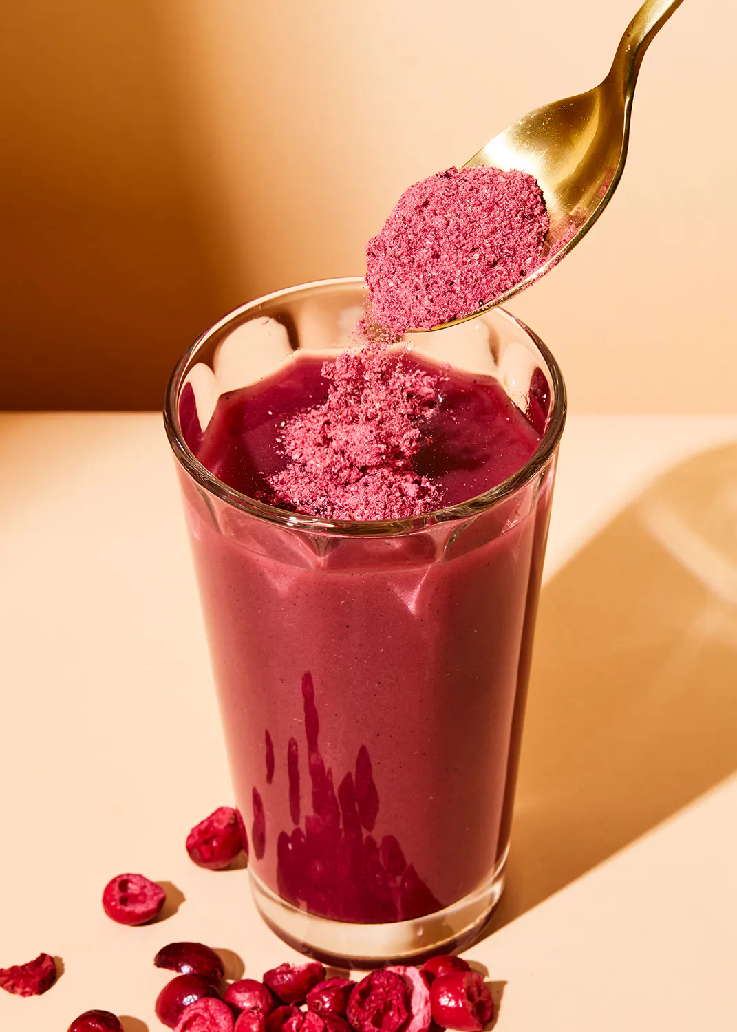 une cuillère de poudre de cranberry est versée dans un smoothie