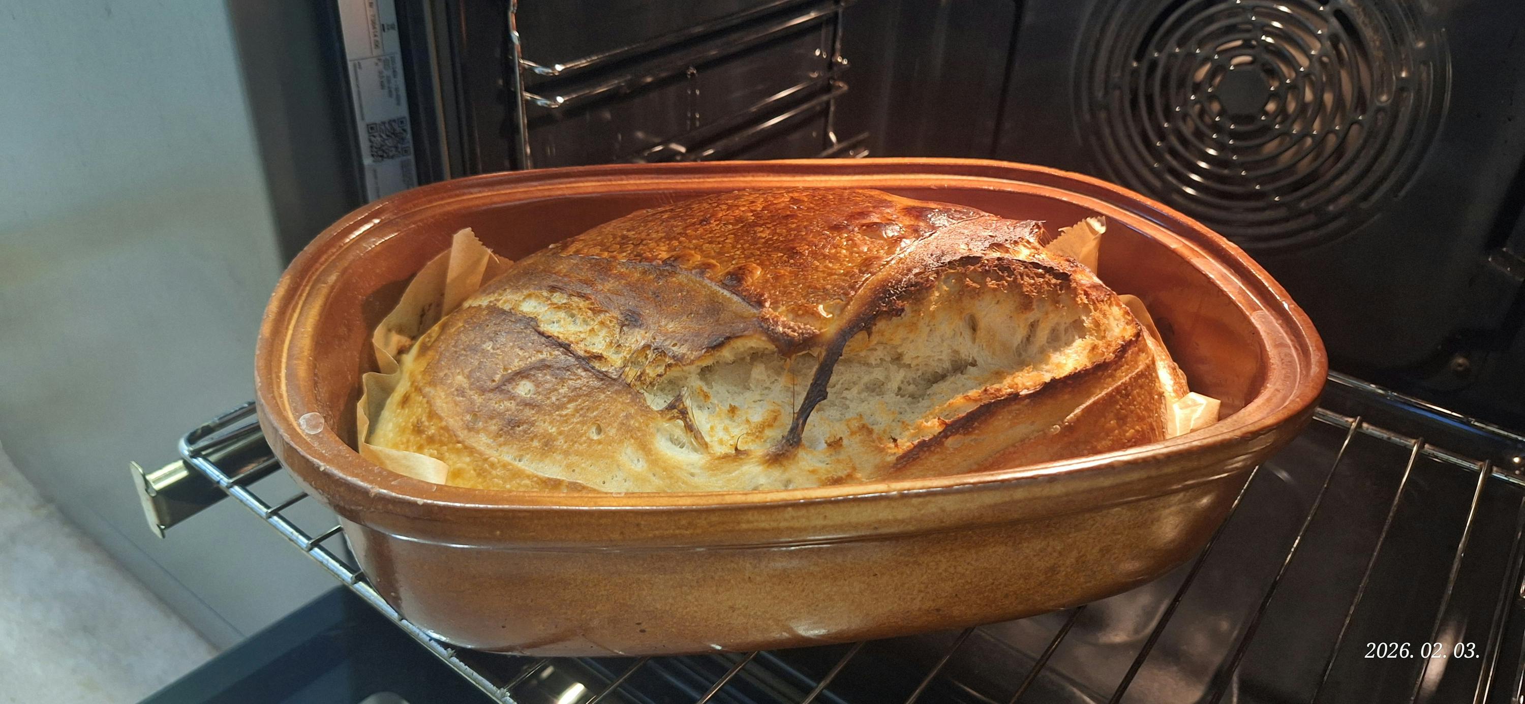 ein laib brot mit goldbrauner kruste backt in einem tontopf im ofen.