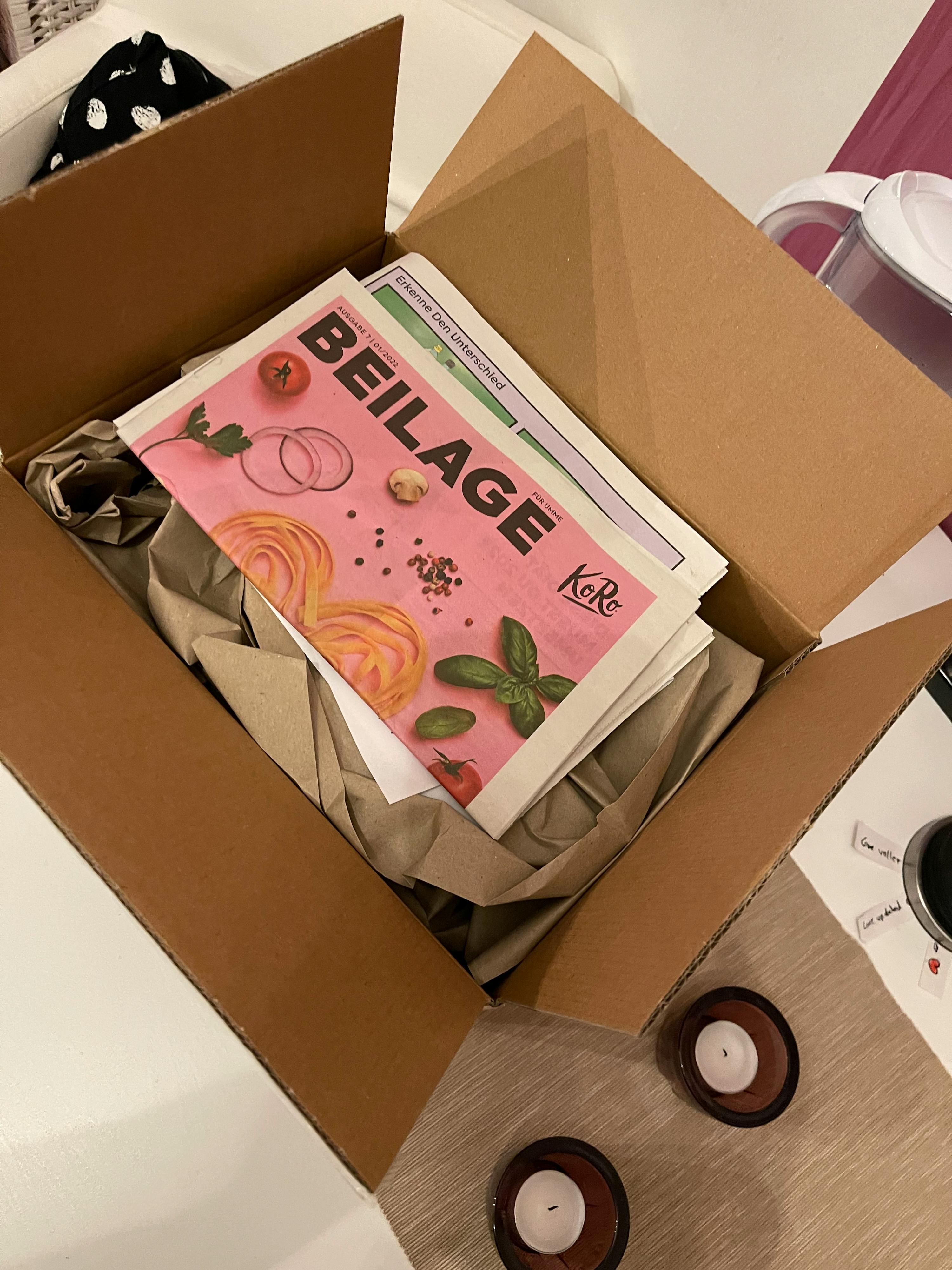 una scatola di cartone è aperta e dentro c'è un giornale rosa con l' etichetta beilage