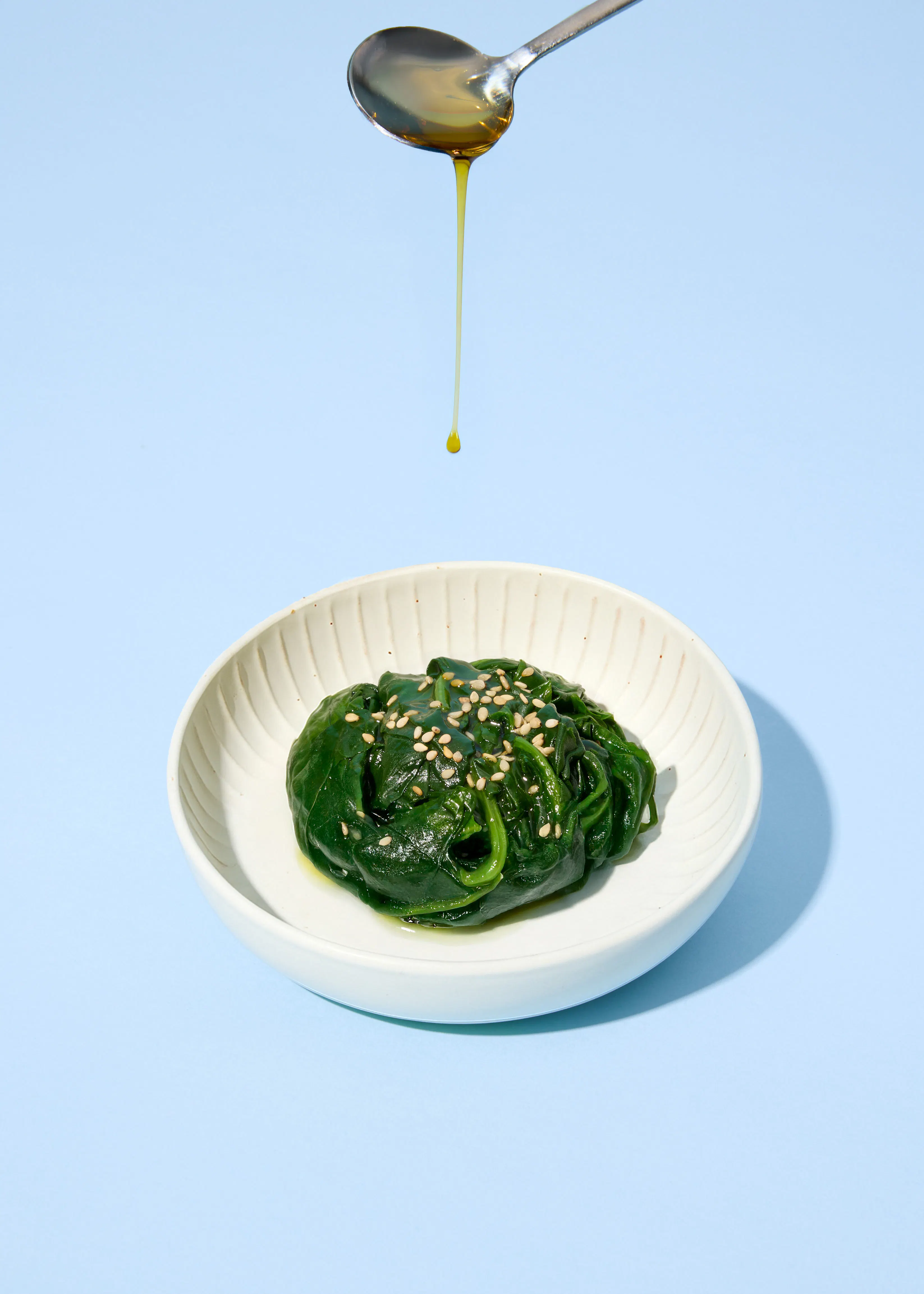 une cuillère verse de l' huile sur une assiette de légumes verts