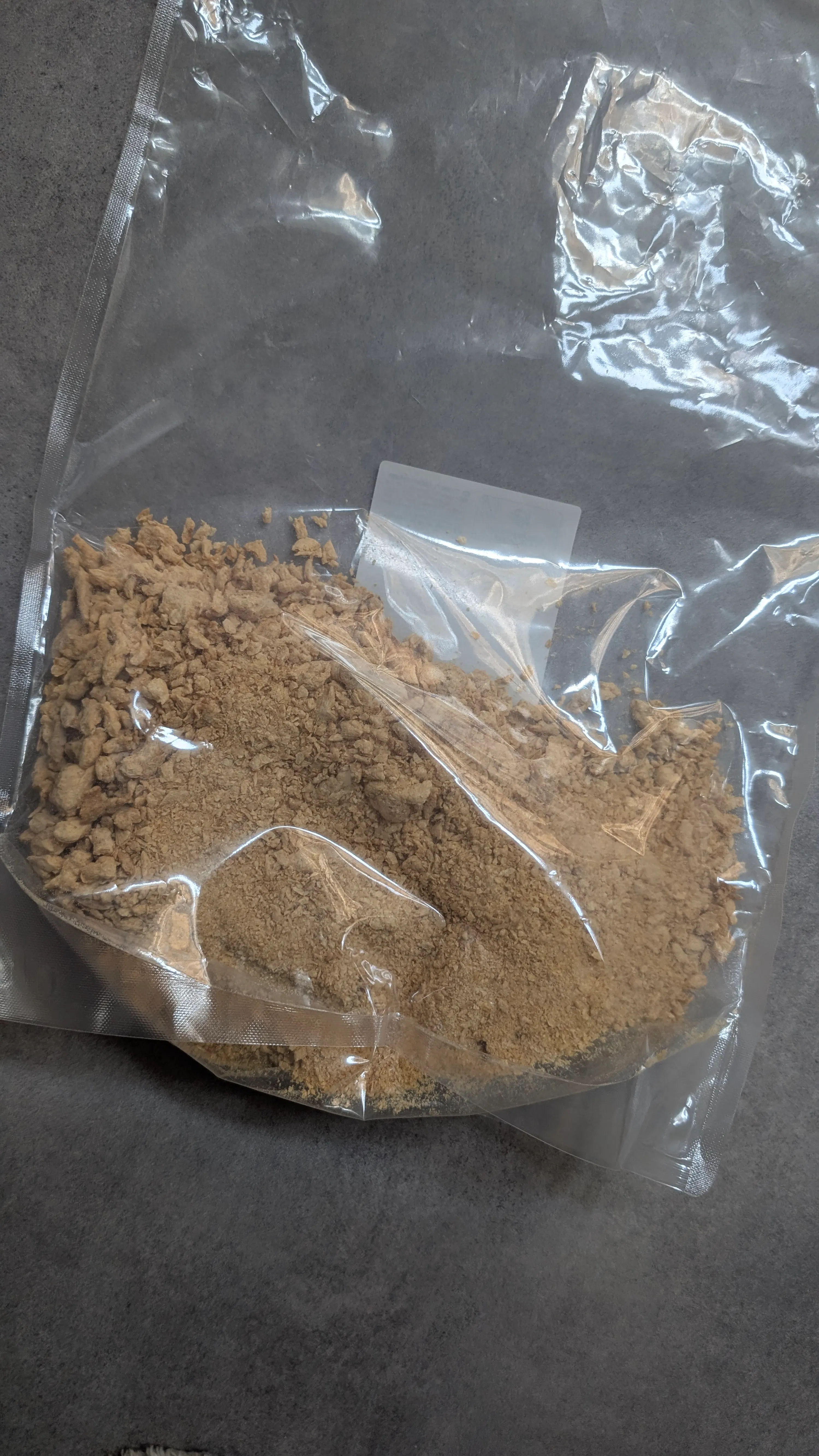 eine durchsichtige plastiktüte, gefüllt mit einer hellbraunen, körnigen substanz, liegt auf einer dunkelgrauen oberfläche.
