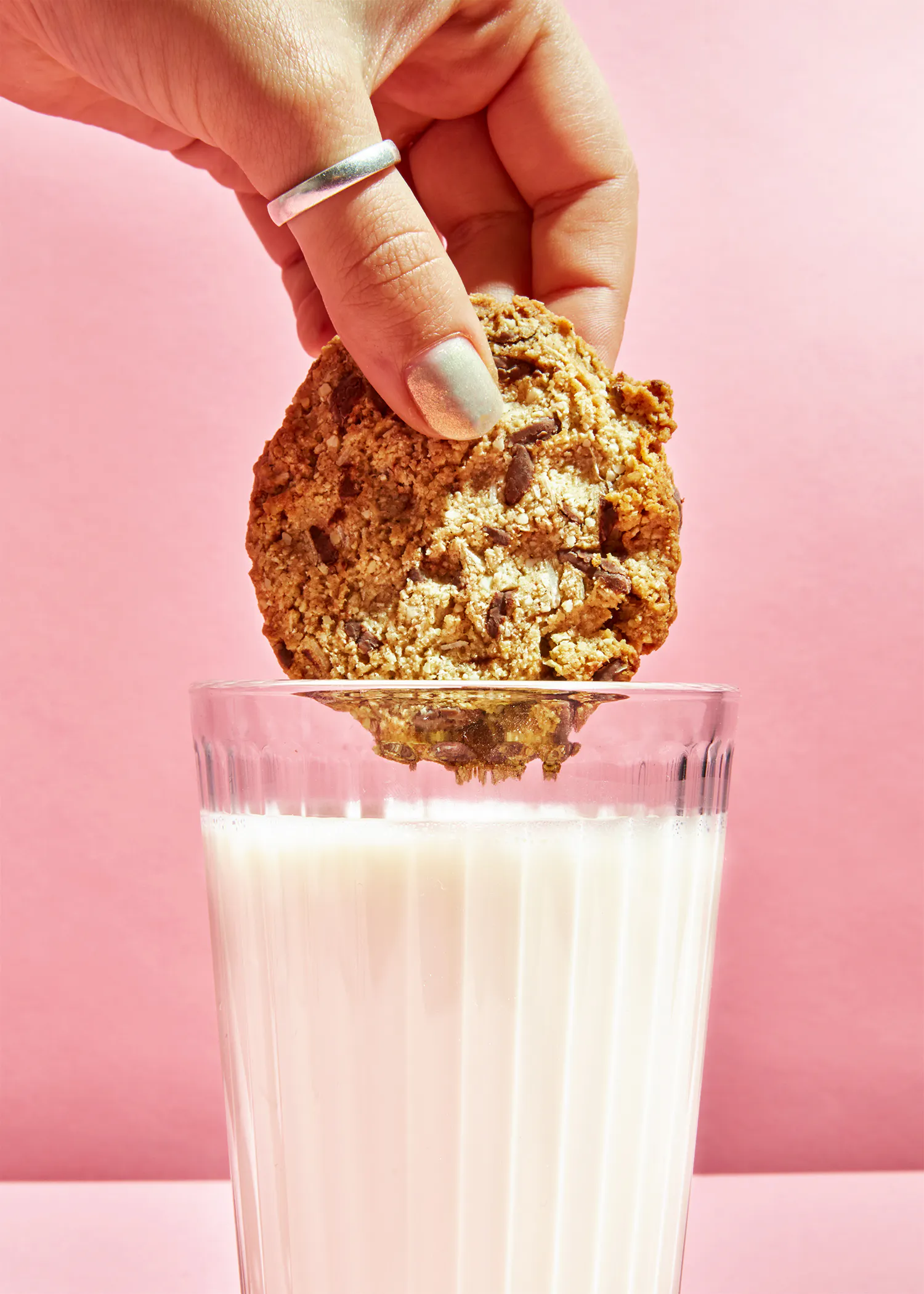 une main tient un biscuit au chocolat au-dessus d' un verre de lait