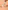 une main tient un emballage de barre protéinée koro avec une illustration de la barre coupée, tandis que deux moitiés de barre chocolatée et des cacahuètes entières et décortiquées sont posées sur une surface beige.