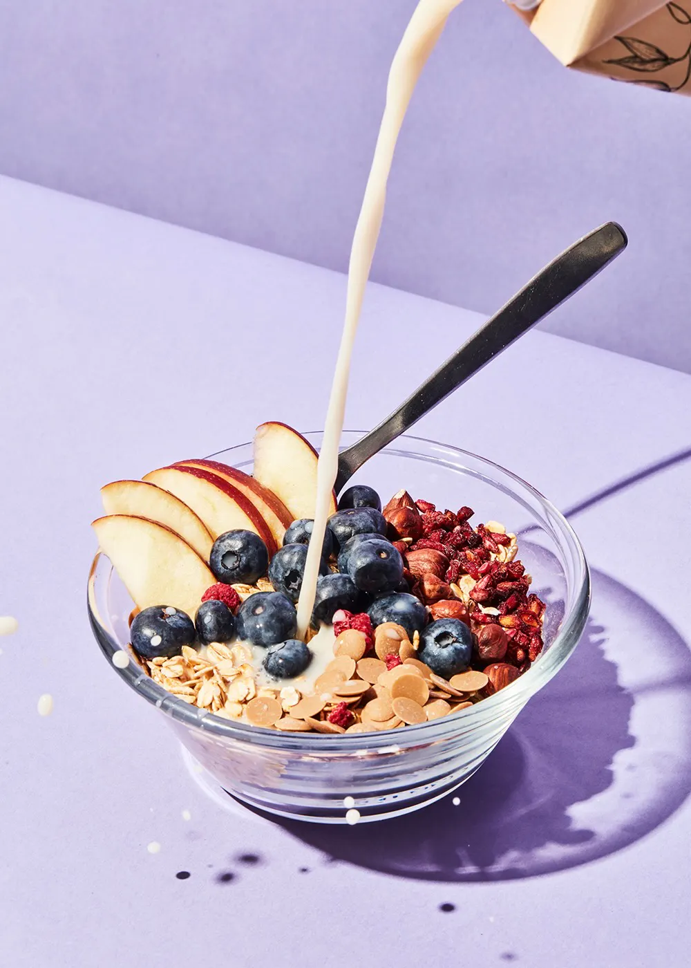 une personne verse du lait dans un bol de céréales avec des fruits et des noix