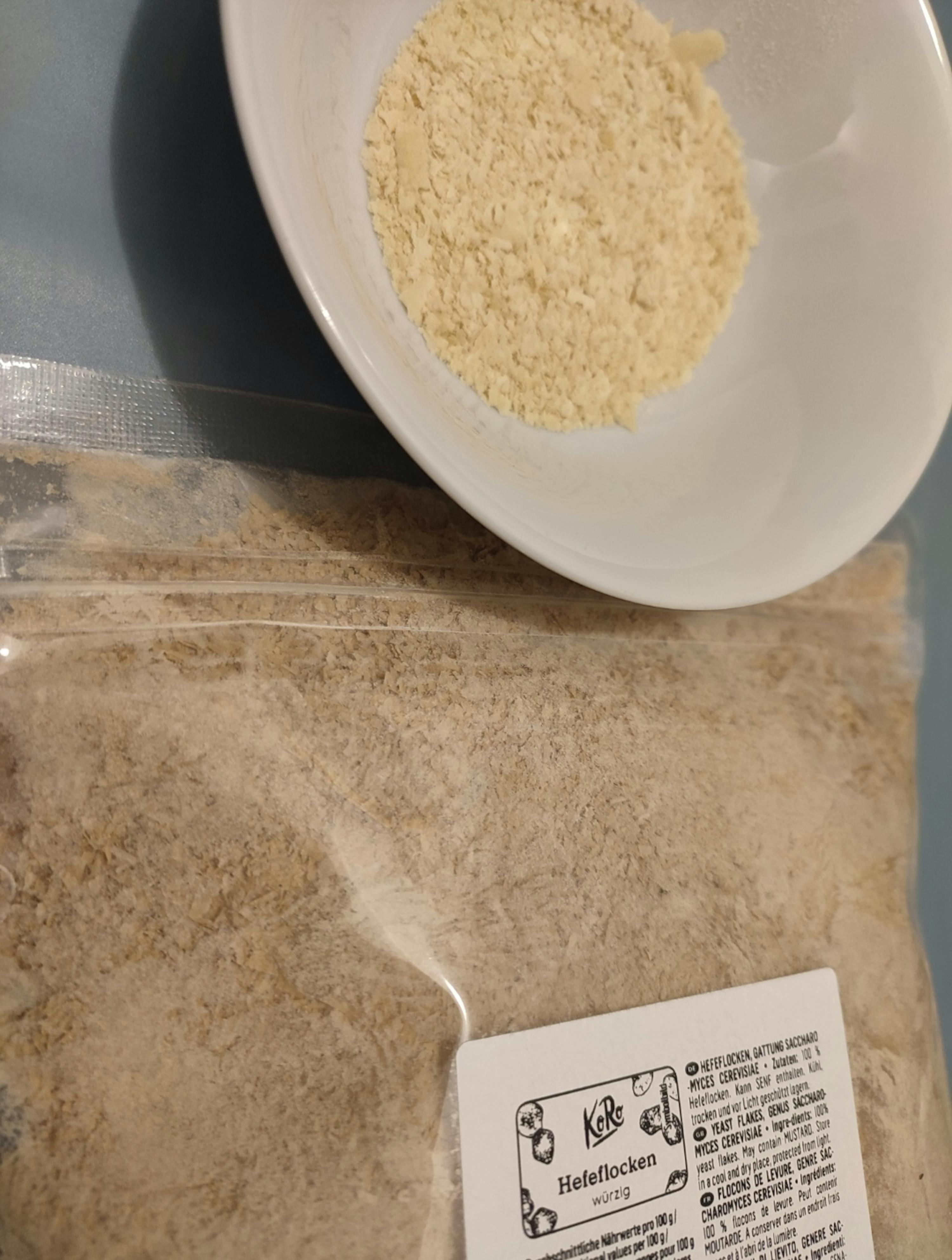 fiocchi di lievito alimentare in una ciotola bianca e in un sacchetto trasparente con etichetta.