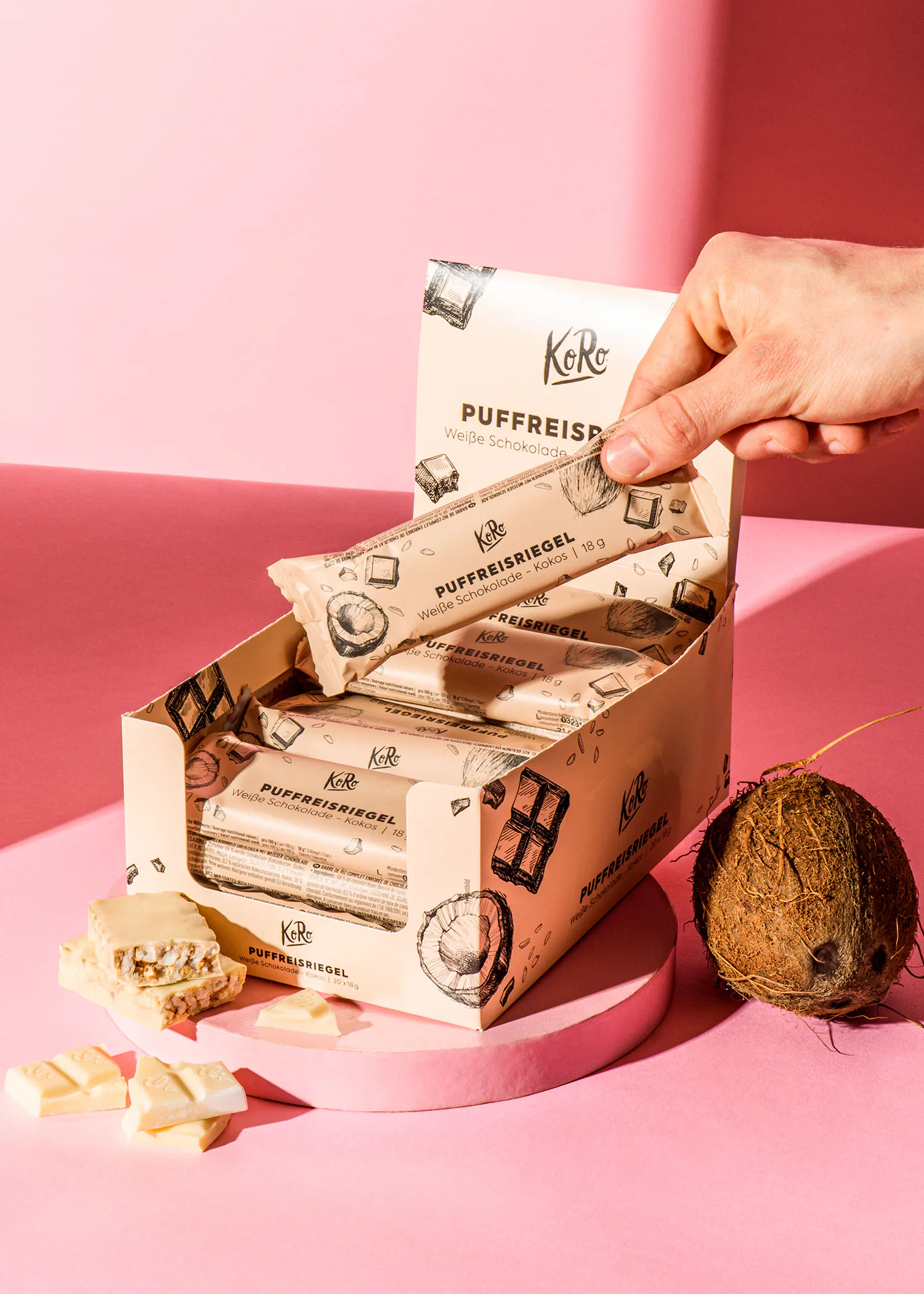 eine Person hält eine Schachtel Kekse mit Kokosnuss auf einem rosa Tisch