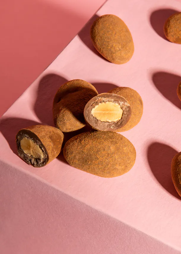a stack of chocolate covered almonds on a pink surface