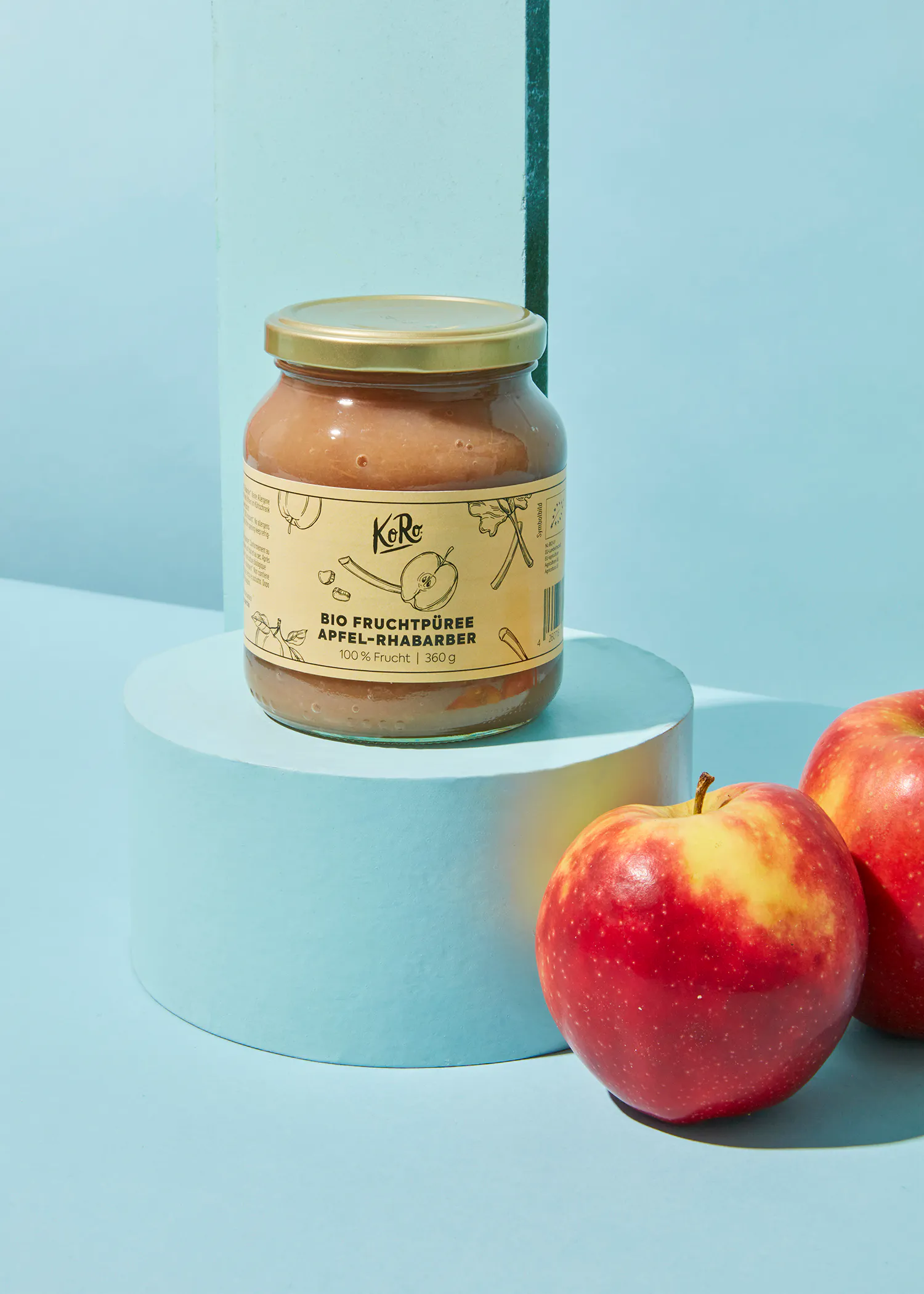 ein Glas fruchtpüree steht auf einem weißen Sockel neben zwei Äpfeln