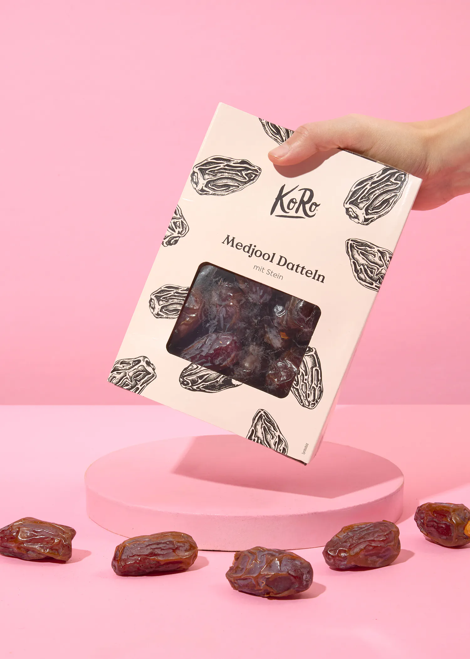 une personne tient une boîte de medjool dattein sur fond rose